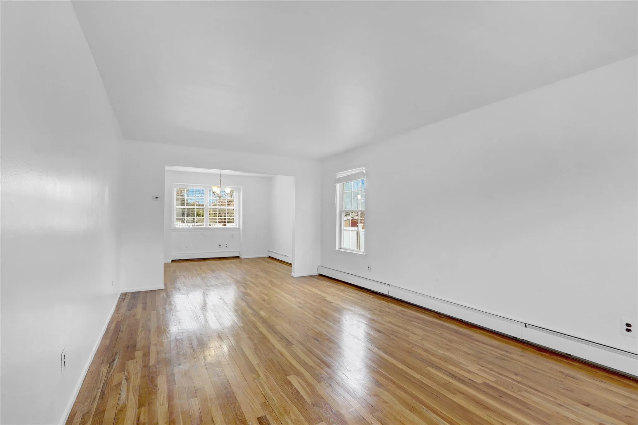 Unfurnished room featuring a chandelier, baseboard heating, and light wood finished floors Unfurnished room featuring a chandelier, baseboard heating, and light wood finished floors