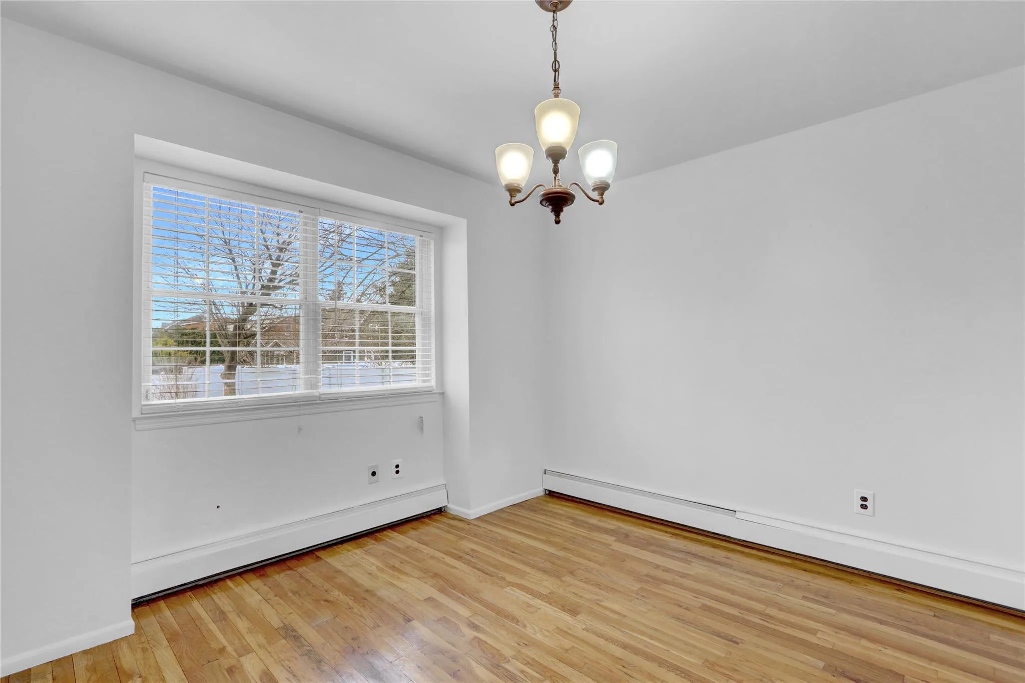 Unfurnished room featuring a baseboard heating unit, a chandelier, and light wood-style flooring Unfurnished room featuring a baseboard heating unit, a chandelier, and light wood-style flooring