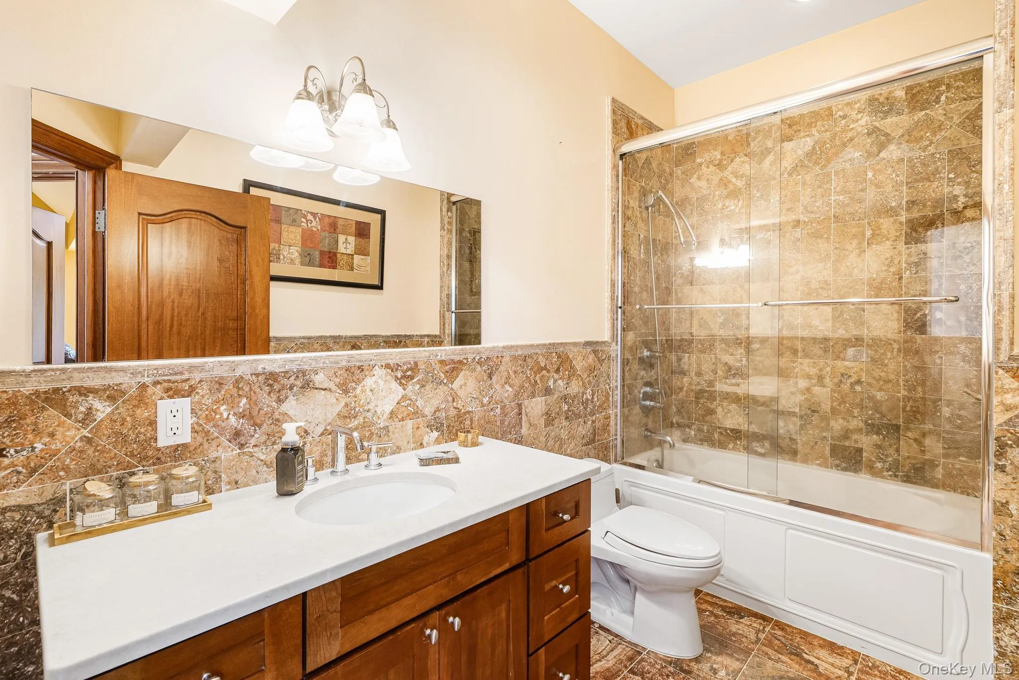 Bathroom featuring a chandelier, vanity, enclosed tub / shower combo, and tile walls Bathroom featuring a chandelier, vanity, enclosed tub / shower combo, and tile walls