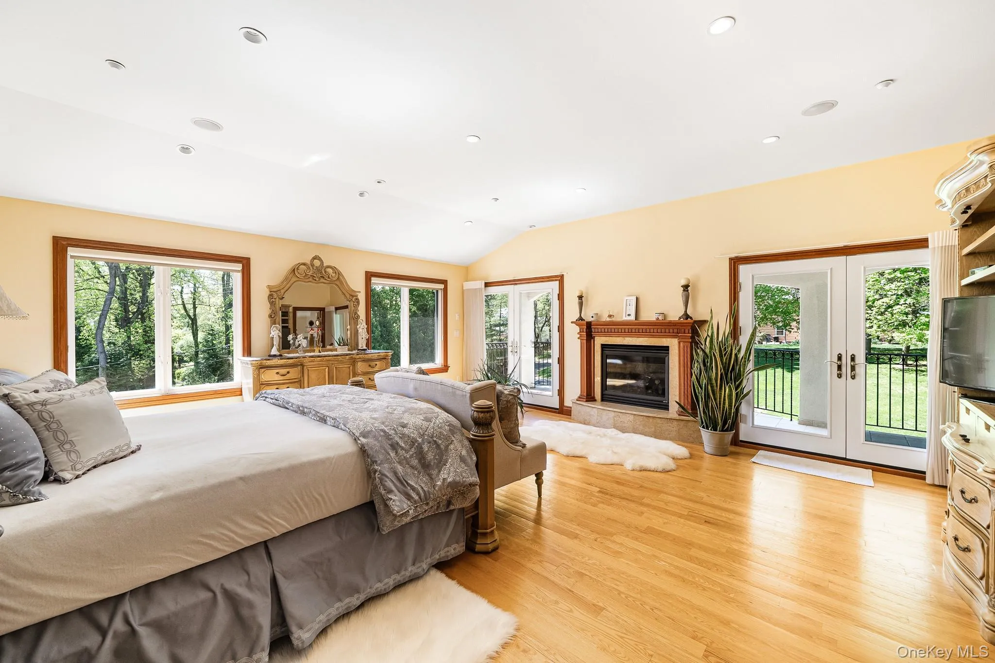 Bedroom with light wood-type flooring, access to outside, lofted ceiling, a fireplace, and recessed lighting Bedroom with light wood-type flooring, access to outside, lofted ceiling, a fireplace, and recessed lighting