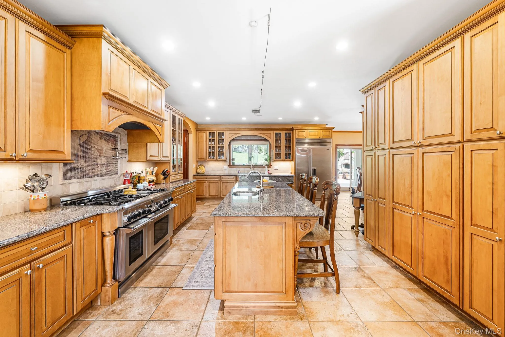 Kitchen featuring high quality appliances, backsplash, light stone countertops, a breakfast bar, and glass insert cabinets Kitchen featuring high quality appliances, backsplash, light stone countertops, a breakfast bar, and glass insert cabinets