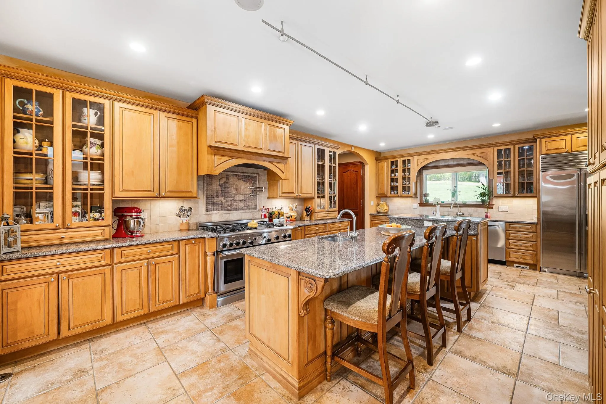 Kitchen featuring high quality appliances, arched walkways, recessed lighting, a center island with sink, and light stone countertops Kitchen featuring high quality appliances, arched walkways, recessed lighting, a center island with sink, and light stone countertops