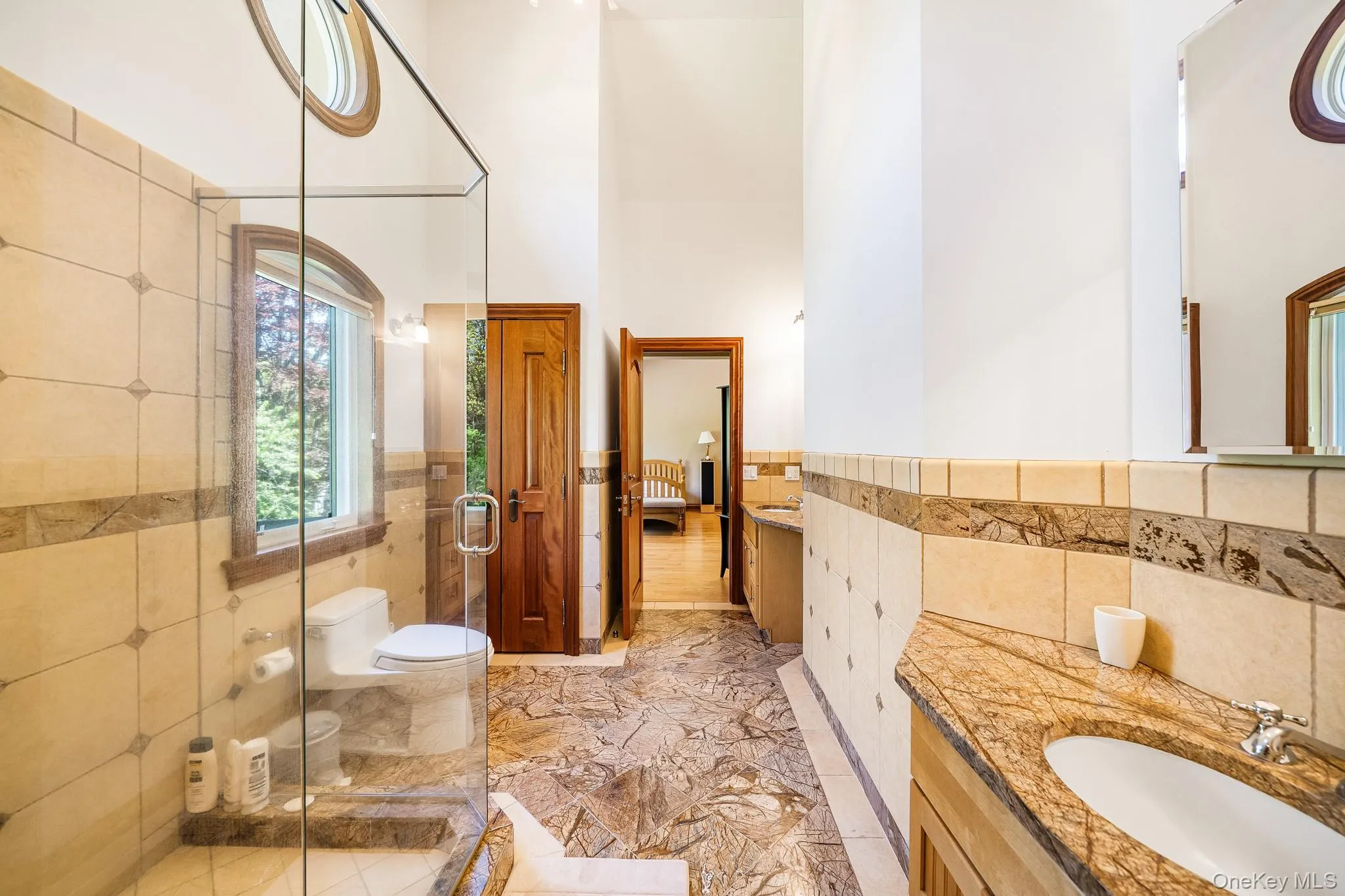 Bathroom featuring tile walls, vanity, a towering ceiling, marble tiled flooring, and a stall shower Bathroom featuring tile walls, vanity, a towering ceiling, marble tiled flooring, and a stall shower