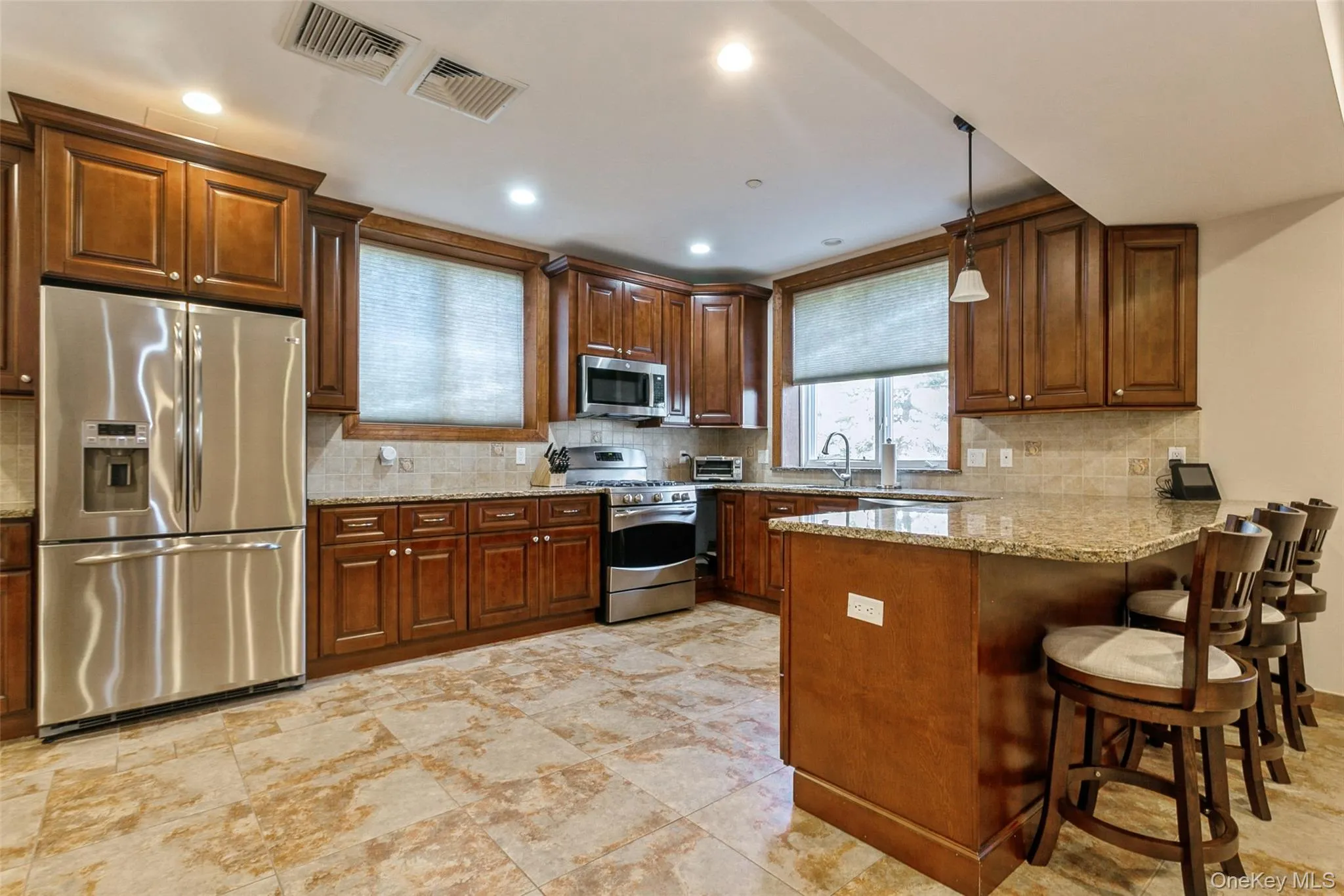 Kitchen with appliances with stainless steel finishes, a peninsula, decorative backsplash, a kitchen breakfast bar, and recessed lighting Kitchen with appliances with stainless steel finishes, a peninsula, decorative backsplash, a kitchen breakfast bar, and recessed lighting