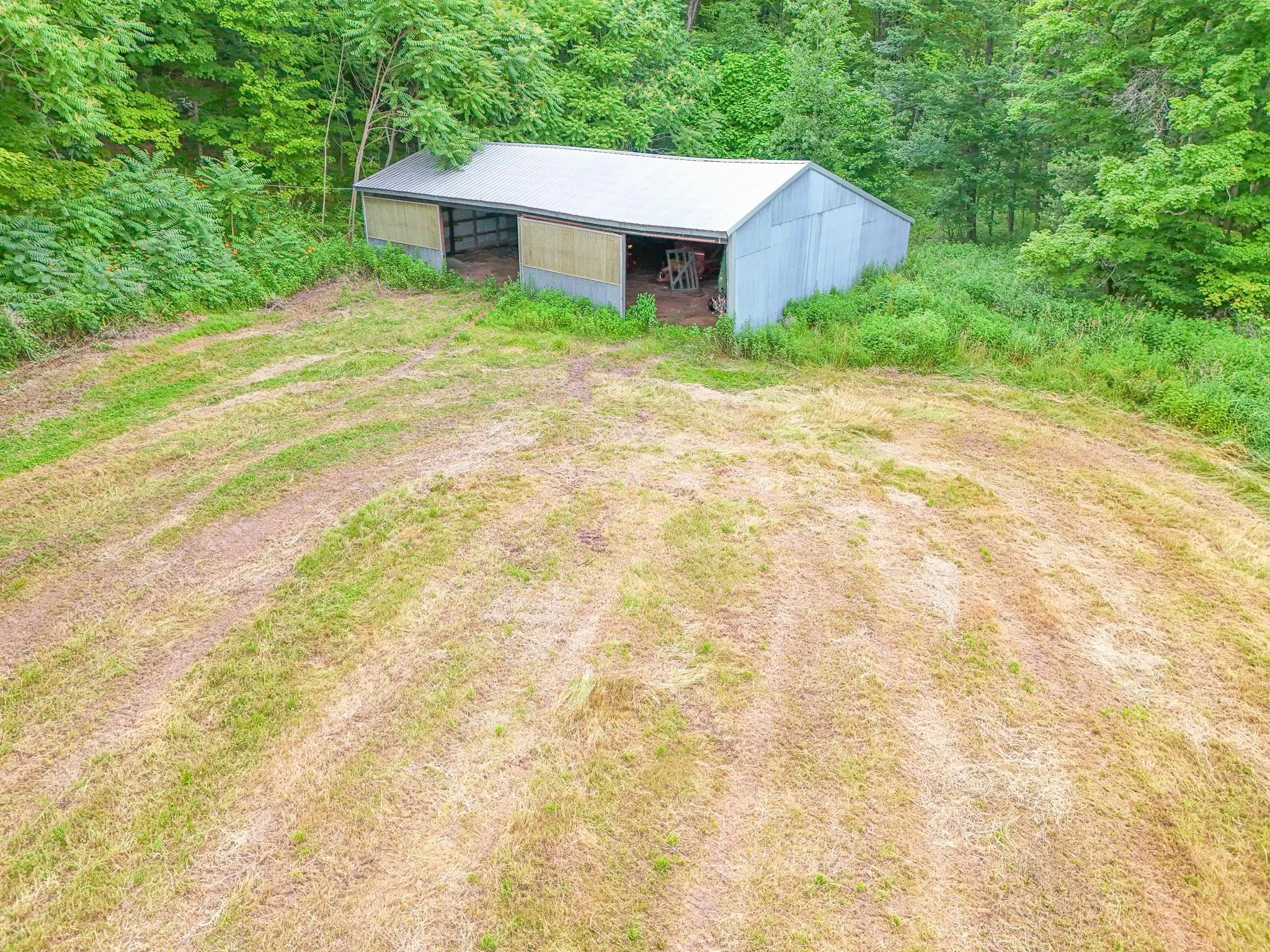 View of yard featuring a pole building, driveway, an outdoor structure, a carport, and a forest view View of yard featuring a pole building, driveway, an outdoor structure, a carport, and a forest view