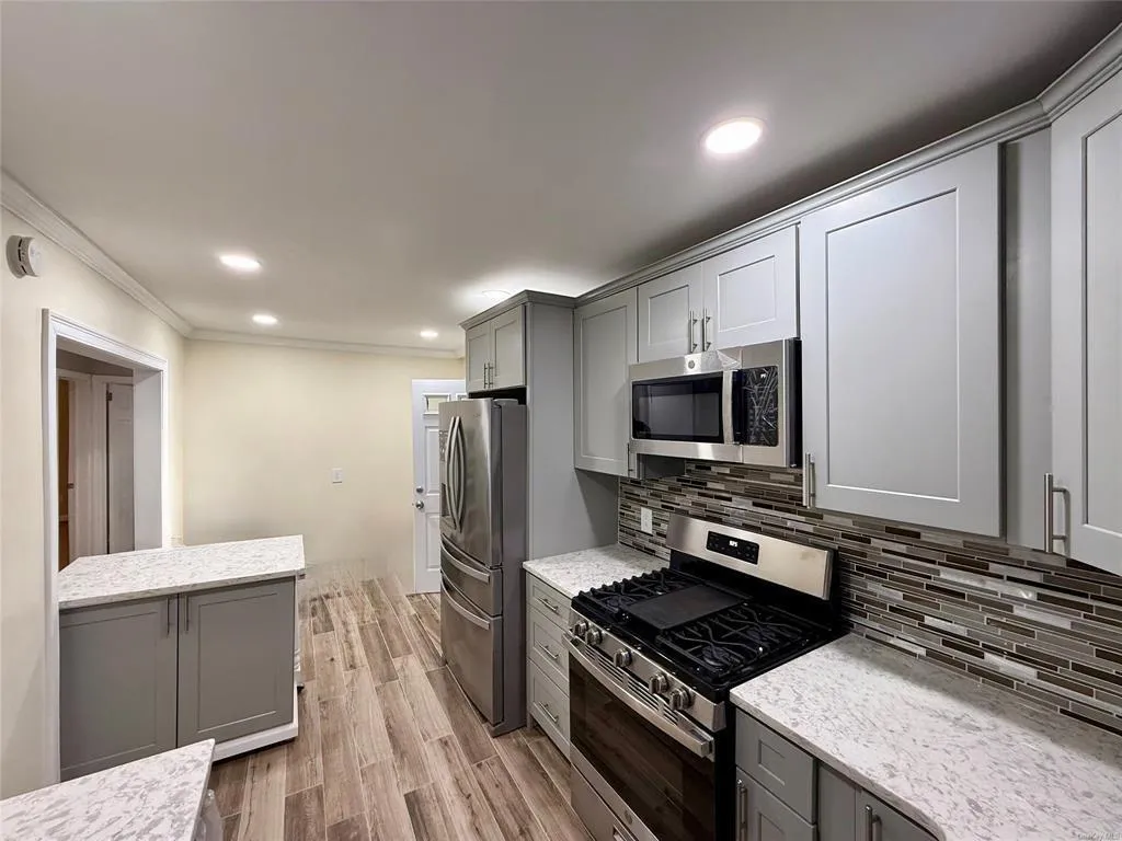 Kitchen with stainless steel appliances, gray cabinets, ornamental molding, decorative backsplash, and light wood finished floors Kitchen with stainless steel appliances, gray cabinets, ornamental molding, decorative backsplash, and light wood finished floors