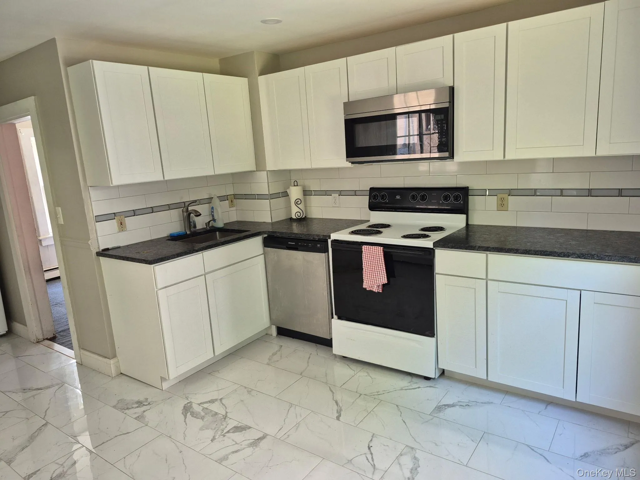 Kitchen with appliances with stainless steel finishes, decorative backsplash, white cabinets, and light marble finish floors Kitchen with appliances with stainless steel finishes, decorative backsplash, white cabinets, and light marble finish floors