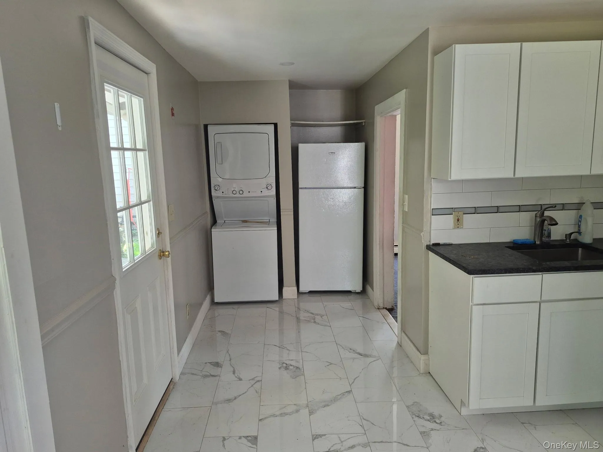 Kitchen featuring light marble finish floors, freestanding refrigerator, white cabinets, stacked washer / dryer, and backsplash Kitchen featuring light marble finish floors, freestanding refrigerator, white cabinets, stacked washer / dryer, and backsplash