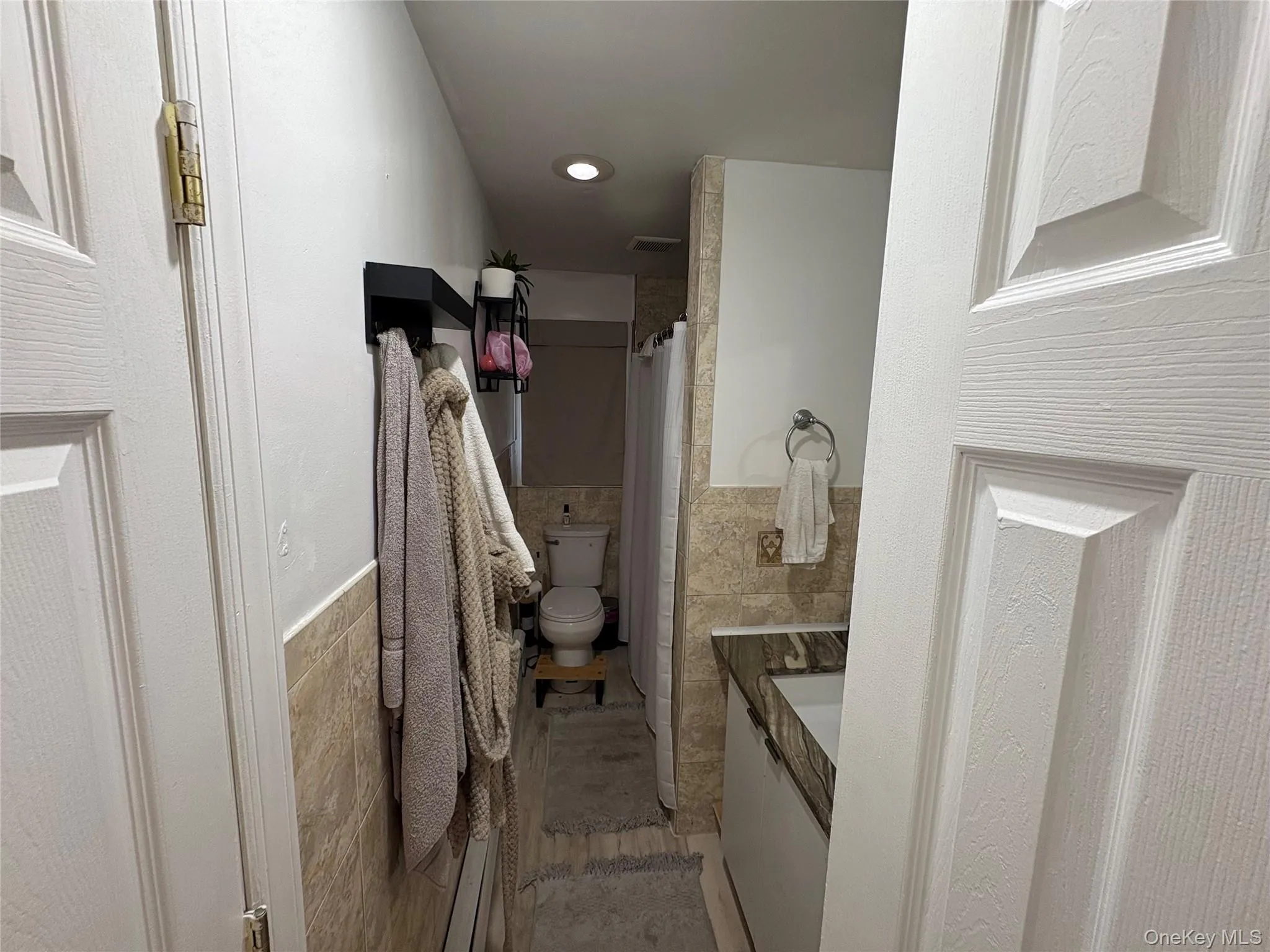 Full bathroom featuring tile walls, a wainscoted wall, vanity, and curtained shower Full bathroom featuring tile walls, a wainscoted wall, vanity, and curtained shower