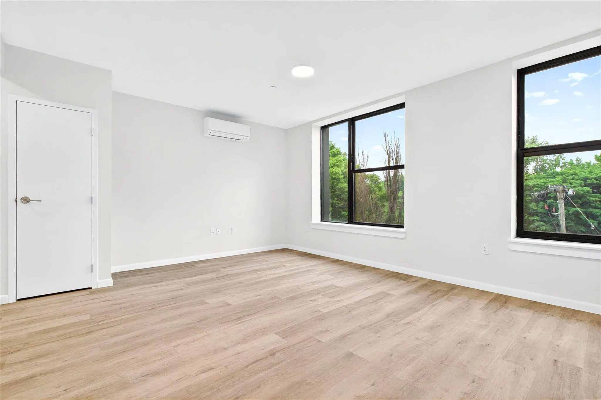 Empty room with a wall unit AC, light wood-style floors, and baseboards Empty room with a wall unit AC, light wood-style floors, and baseboards