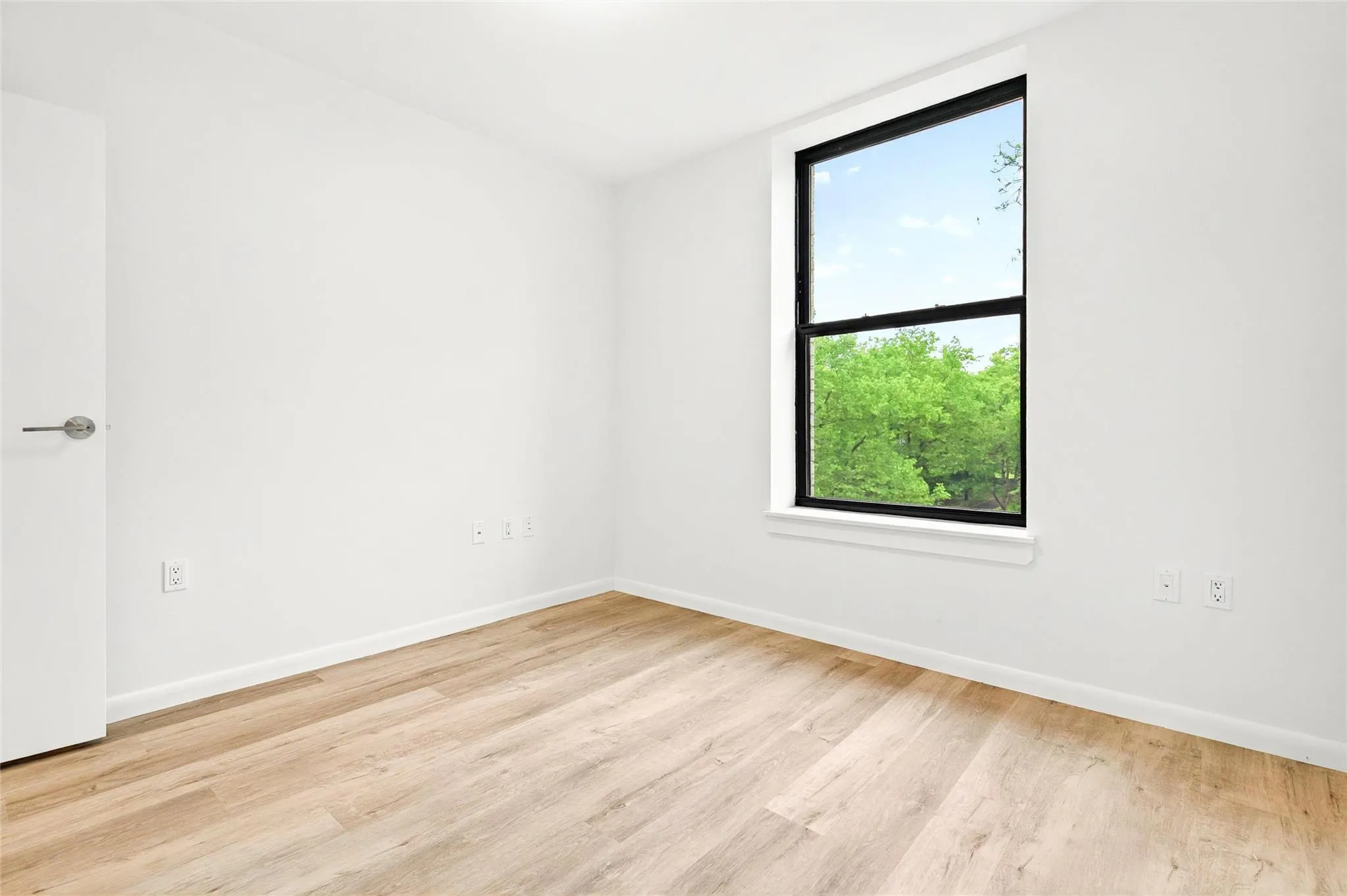 Bedroom with an AC wall unit, light wood finished floors, and baseboards Bedroom with an AC wall unit, light wood finished floors, and baseboards