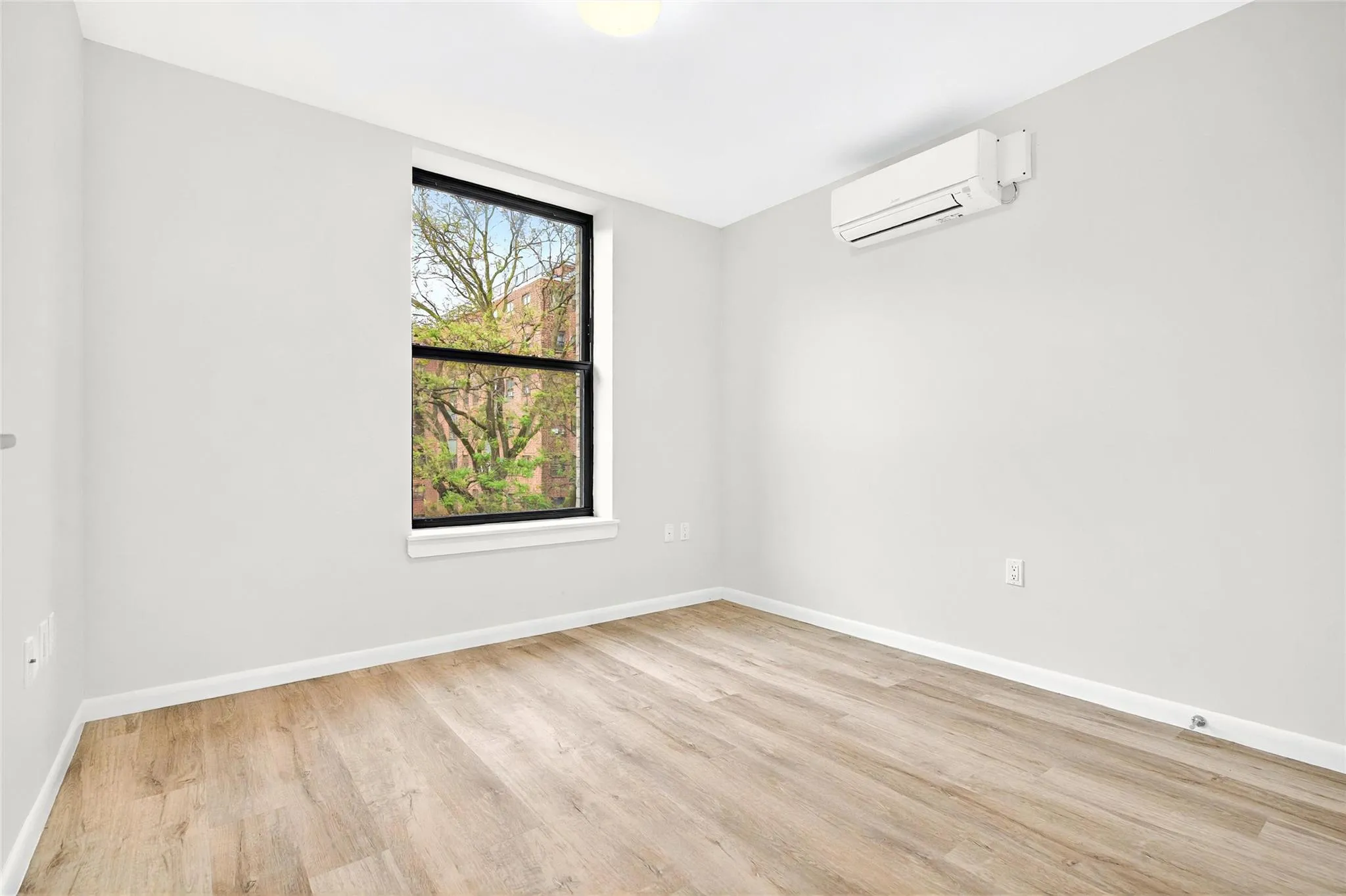 Bedroom with an AC wall unit, light wood finished floors, and baseboards Bedroom with an AC wall unit, light wood finished floors, and baseboards