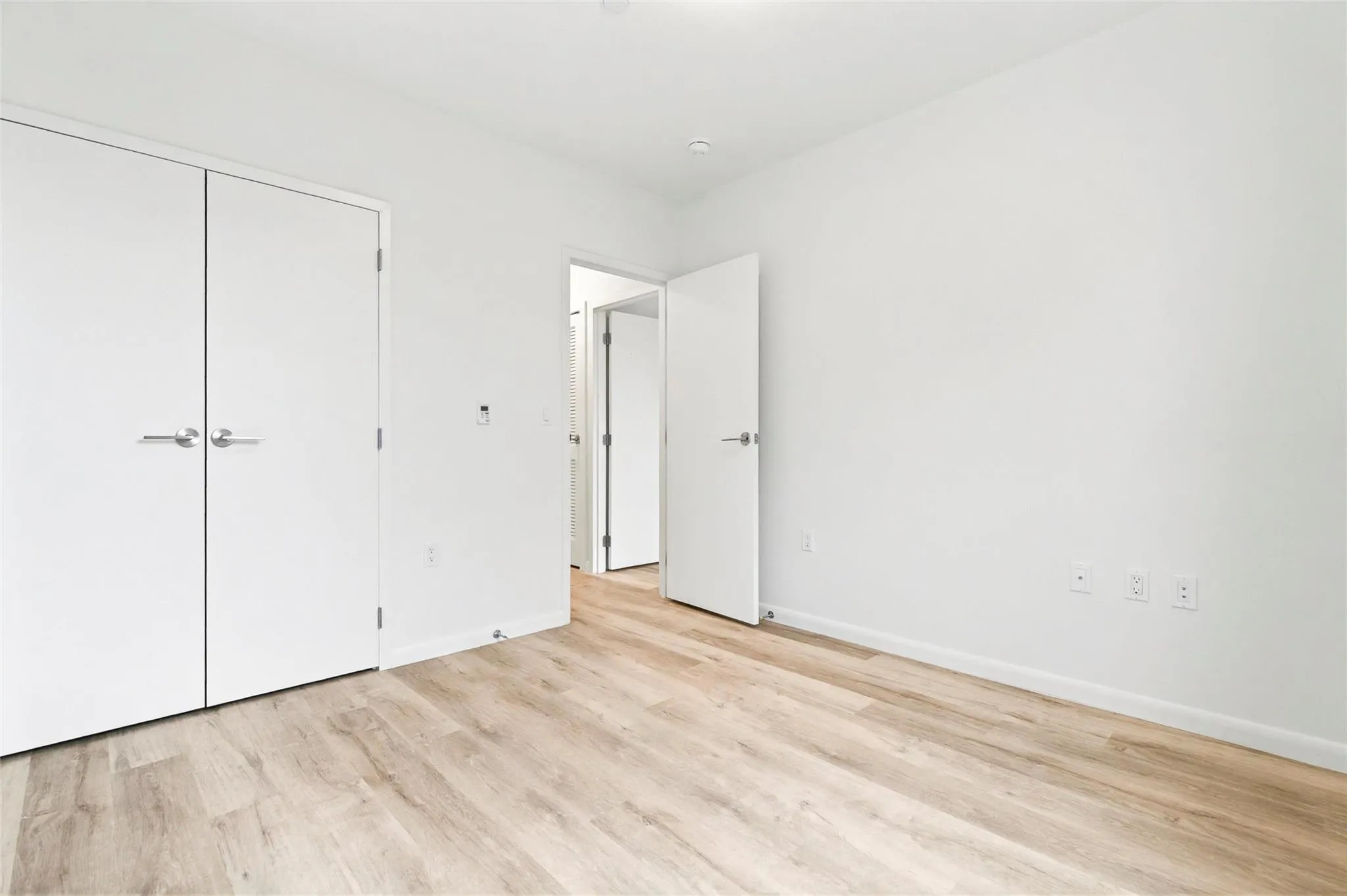 Bedroom with an AC wall unit, light wood finished floors, and baseboards Bedroom with an AC wall unit, light wood finished floors, and baseboards
