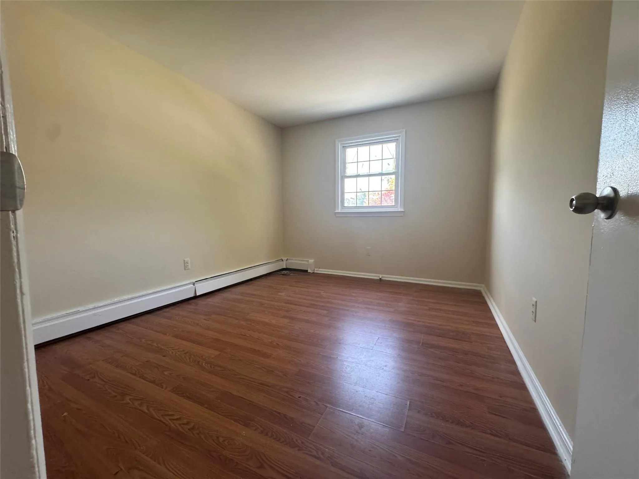 Empty room featuring dark wood-type flooring and a baseboard radiator Empty room featuring dark wood-type flooring and a baseboard radiator
