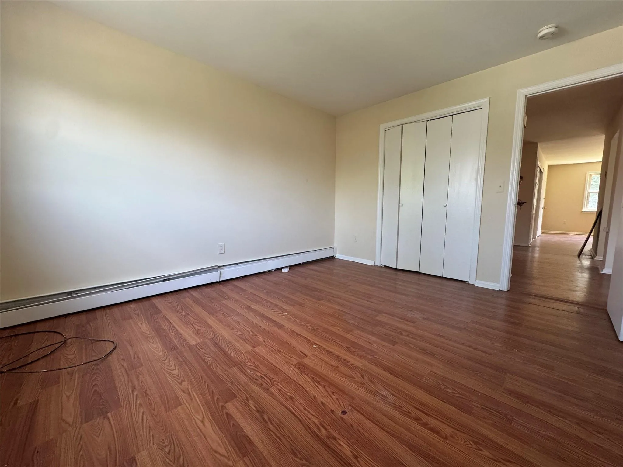 Unfurnished bedroom with a baseboard radiator, wood finished floors, and a closet Unfurnished bedroom with a baseboard radiator, wood finished floors, and a closet