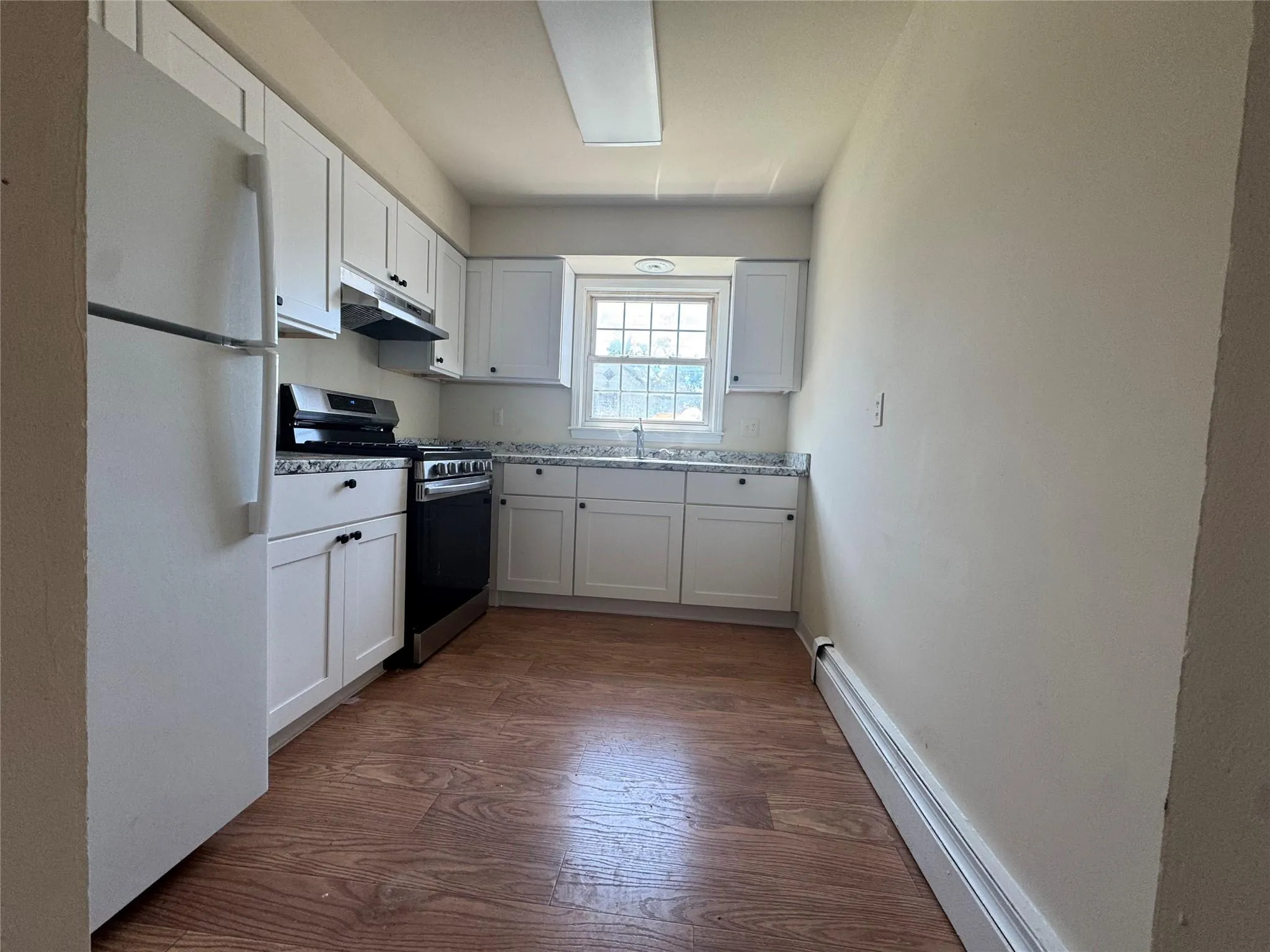 Kitchen with freestanding refrigerator, stainless steel gas range oven, under cabinet range hood, dark wood-style floors, and white cabinets Kitchen with freestanding refrigerator, stainless steel gas range oven, under cabinet range hood, dark wood-style floors, and white cabinets