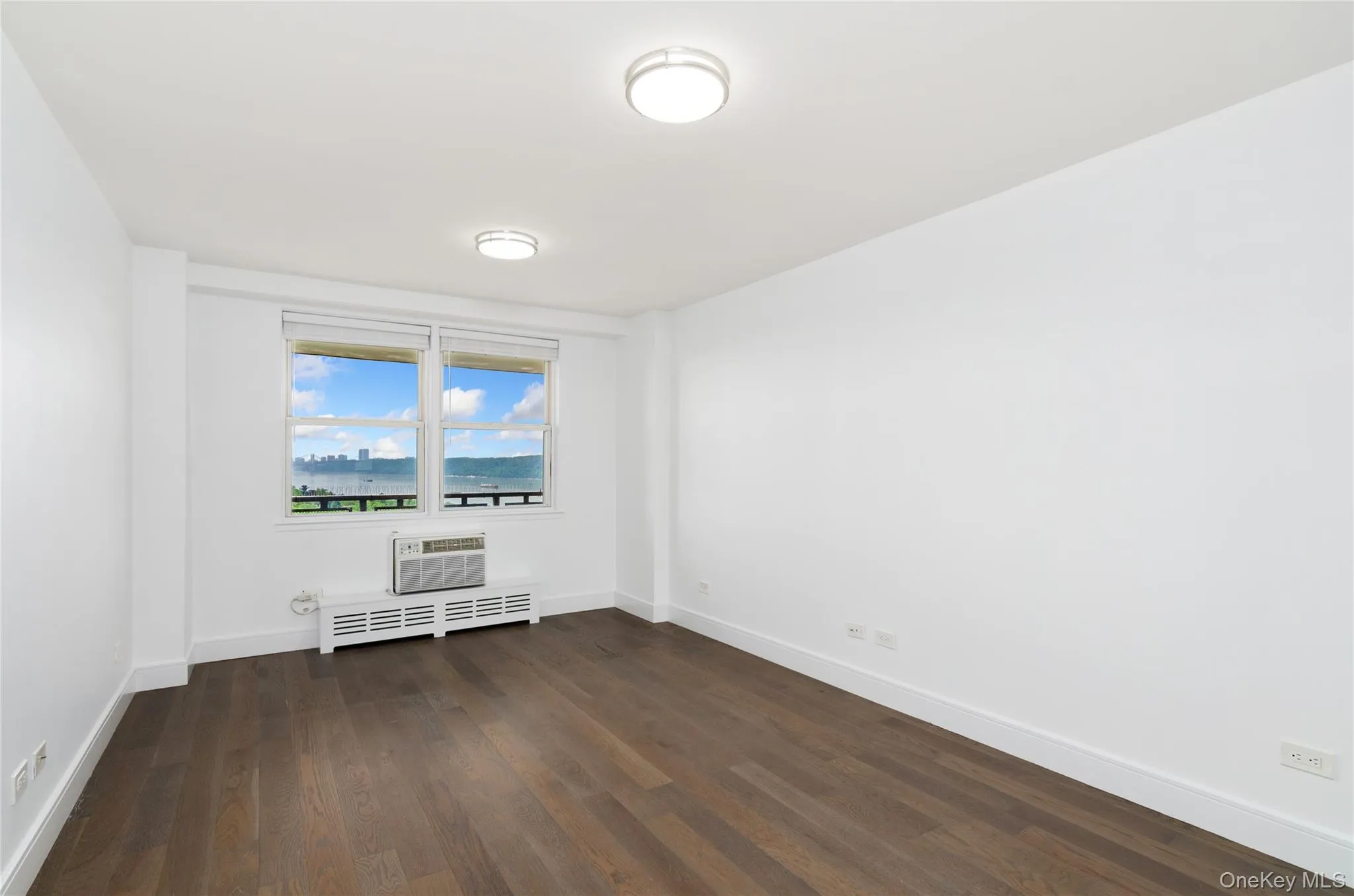 Empty room with dark wood finished floors, radiator heating unit, and an AC wall unit Empty room with dark wood finished floors, radiator heating unit, and an AC wall unit