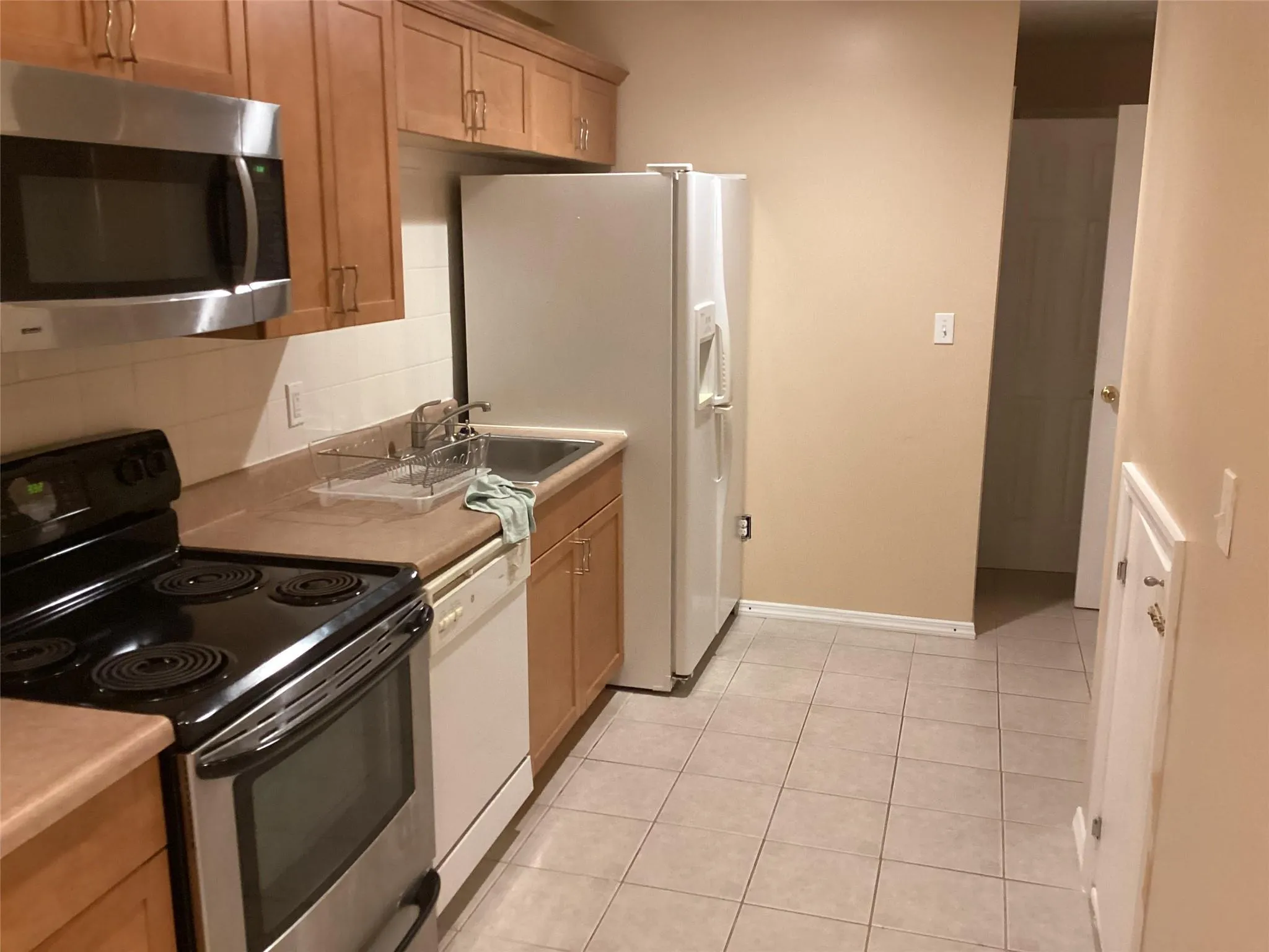 Kitchen with appliances with stainless steel finishes, backsplash, light countertops, and light tile patterned floors Kitchen with appliances with stainless steel finishes, backsplash, light countertops, and light tile patterned floors