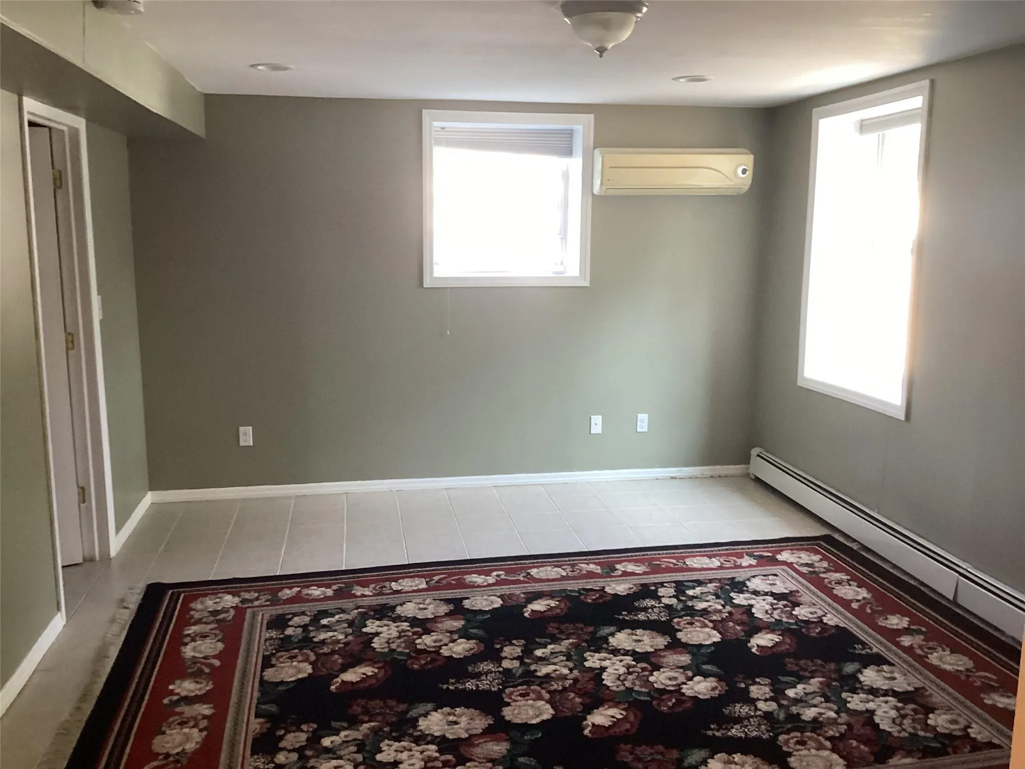 Empty room featuring a wall mounted AC, a baseboard radiator, and light tile patterned flooring Empty room featuring a wall mounted AC, a baseboard radiator, and light tile patterned flooring