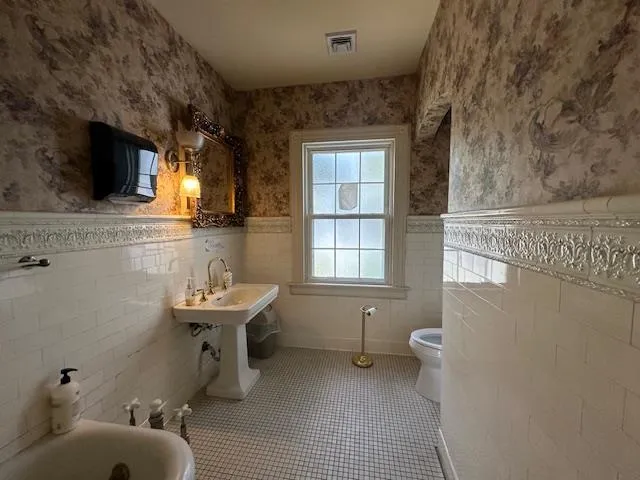 Full bathroom featuring wainscoting, tile walls, tile patterned flooring, wallpapered walls, and a tub to relax in Full bathroom featuring wainscoting, tile walls, tile patterned flooring, wallpapered walls, and a tub to relax in