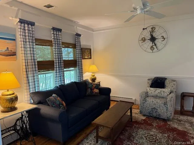 Living area featuring baseboard heating, wood finished floors, and ceiling fan Living area featuring baseboard heating, wood finished floors, and ceiling fan