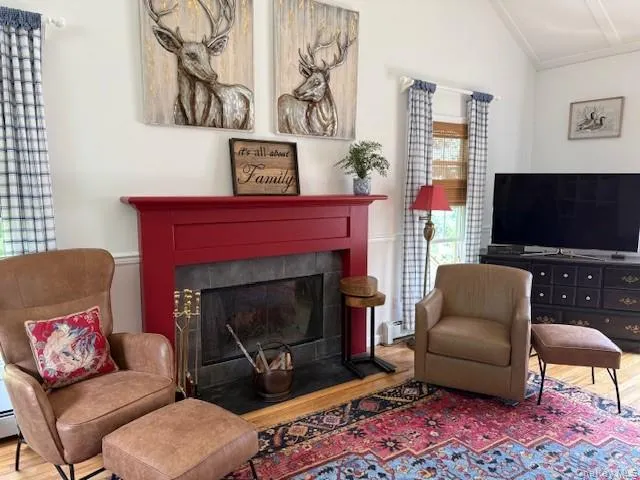Sitting room with vaulted ceiling, wood finished floors, and a tiled fireplace Sitting room with vaulted ceiling, wood finished floors, and a tiled fireplace