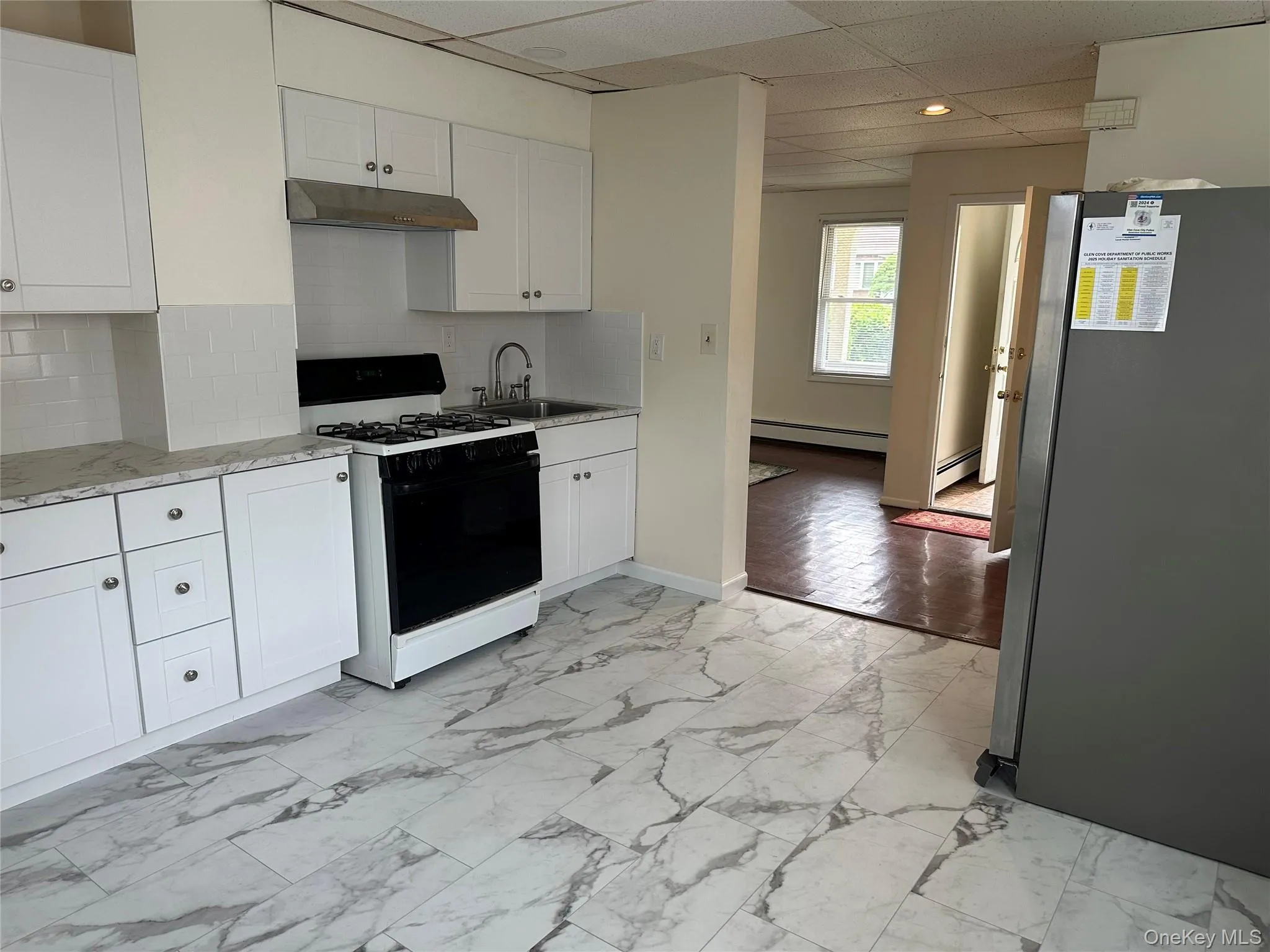 Kitchen featuring black range with gas stovetop, freestanding refrigerator, under cabinet range hood, baseboard heating, and white cabinets Kitchen featuring black range with gas stovetop, freestanding refrigerator, under cabinet range hood, baseboard heating, and white cabinets