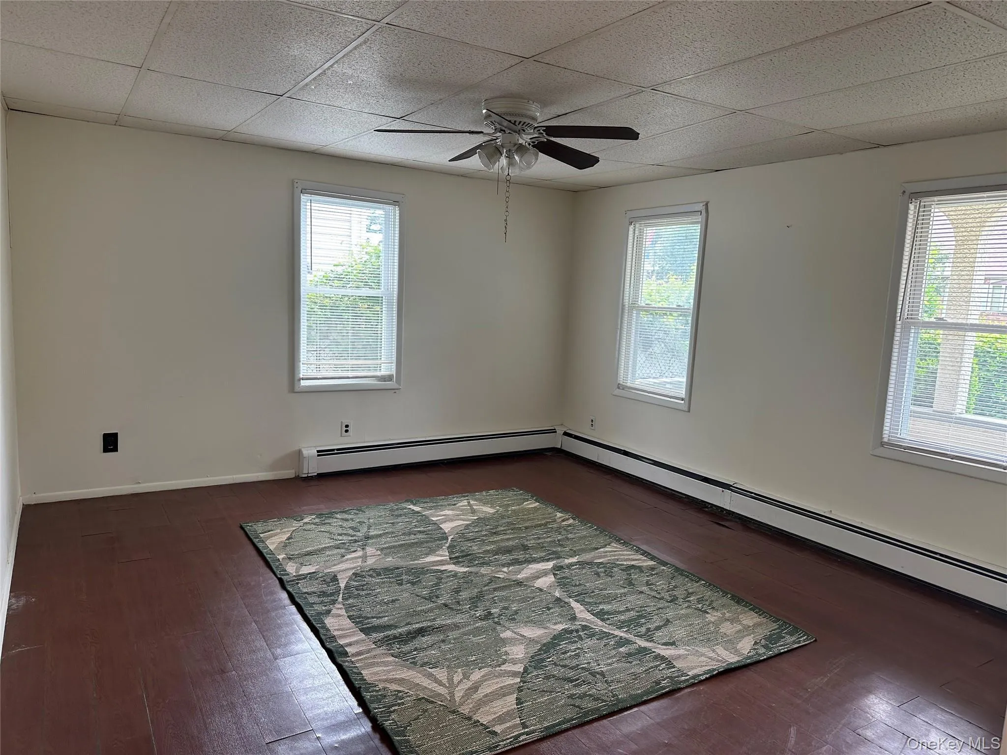 Spare room featuring a ceiling fan, a drop ceiling, wood finished floors, and baseboard heating Spare room featuring a ceiling fan, a drop ceiling, wood finished floors, and baseboard heating