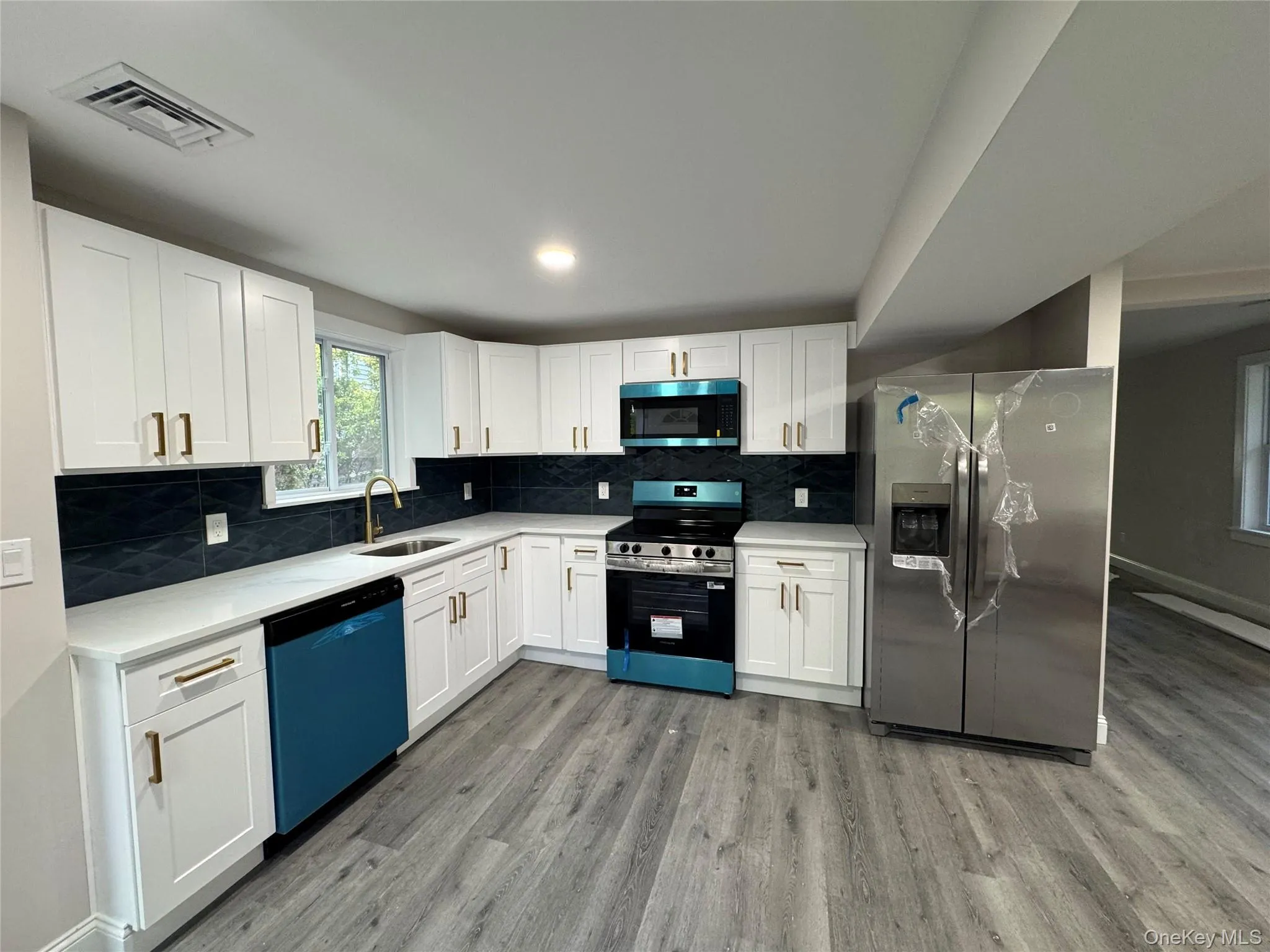 Kitchen with stainless steel appliances, white cabinetry, decorative backsplash, and light wood finished floors Kitchen with stainless steel appliances, white cabinetry, decorative backsplash, and light wood finished floors