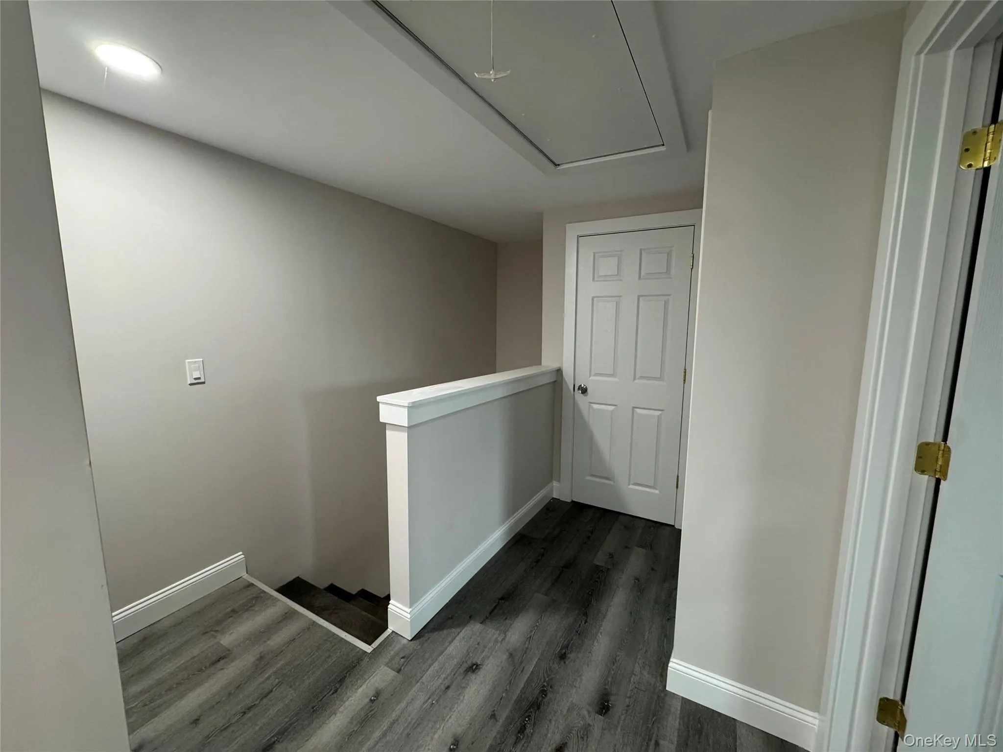 Hallway featuring an upstairs landing, attic access, and dark wood-type flooring Hallway featuring an upstairs landing, attic access, and dark wood-type flooring