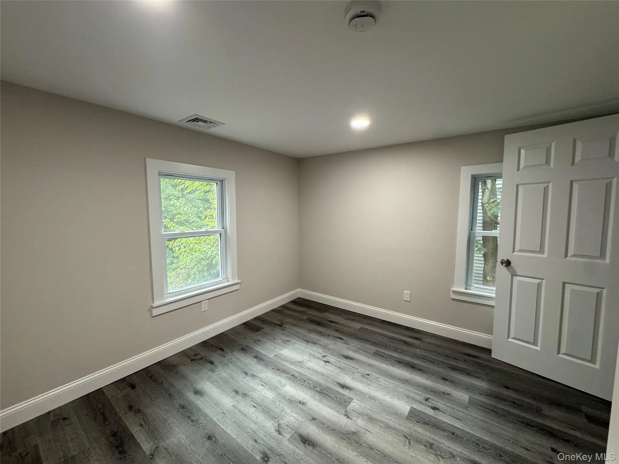 Empty room with dark wood-style floors, plenty of natural light, and recessed lighting Empty room with dark wood-style floors, plenty of natural light, and recessed lighting