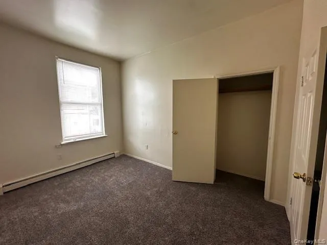 Unfurnished 1st flbedroom with baseboard heating and dark colored carpet Unfurnished 1st flbedroom with baseboard heating and dark colored carpet