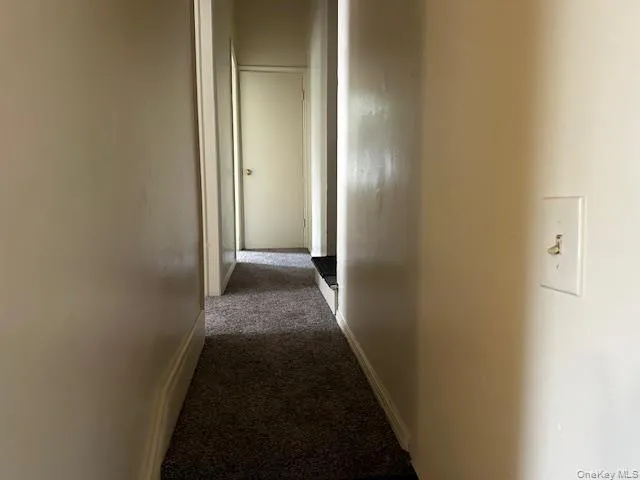 Hall featuring dark carpet and baseboards Hall featuring dark carpet and baseboards