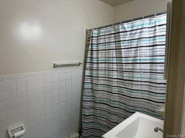 Bathroom featuring tile walls and a shower with shower curtain Bathroom featuring tile walls and a shower with shower curtain
