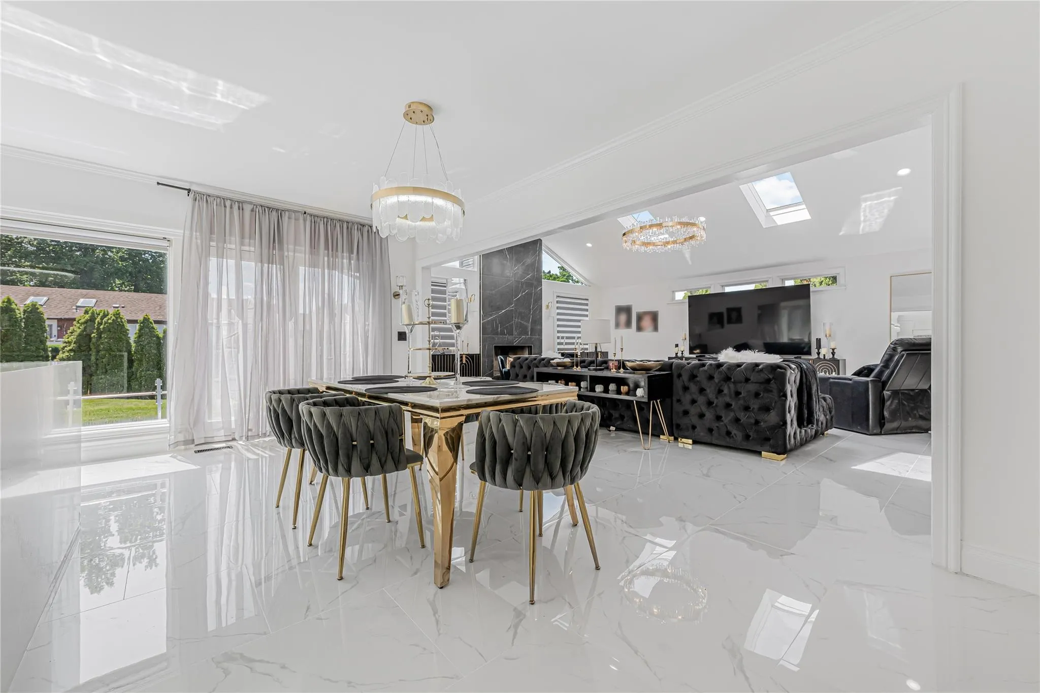 Dining room with a chandelier, light marble finish flooring, a premium fireplace, crown molding, and a skylight Dining room with a chandelier, light marble finish flooring, a premium fireplace, crown molding, and a skylight