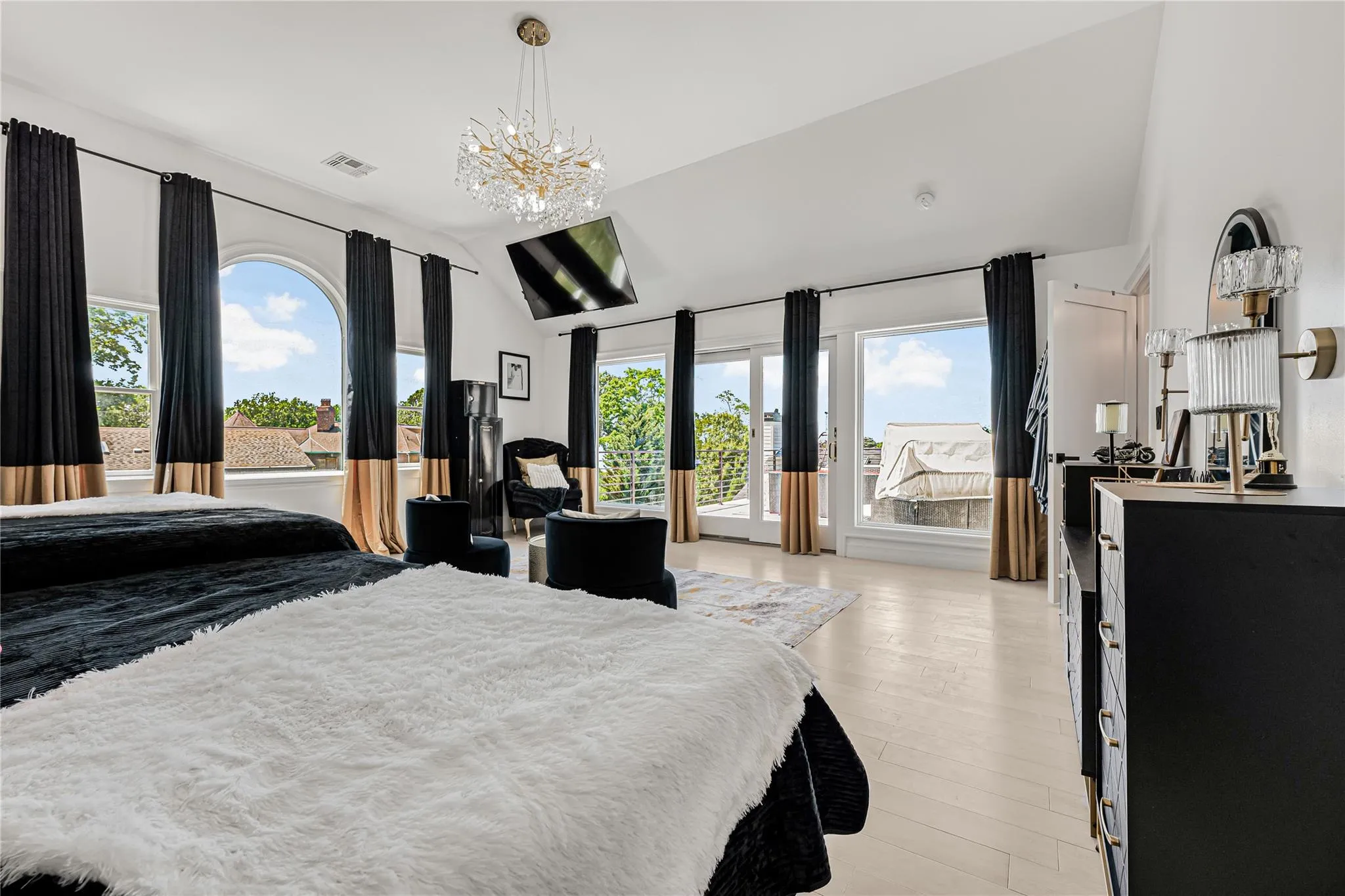 Bedroom featuring lofted ceiling, access to exterior, multiple windows, light wood-type flooring, and a chandelier Bedroom featuring lofted ceiling, access to exterior, multiple windows, light wood-type flooring, and a chandelier