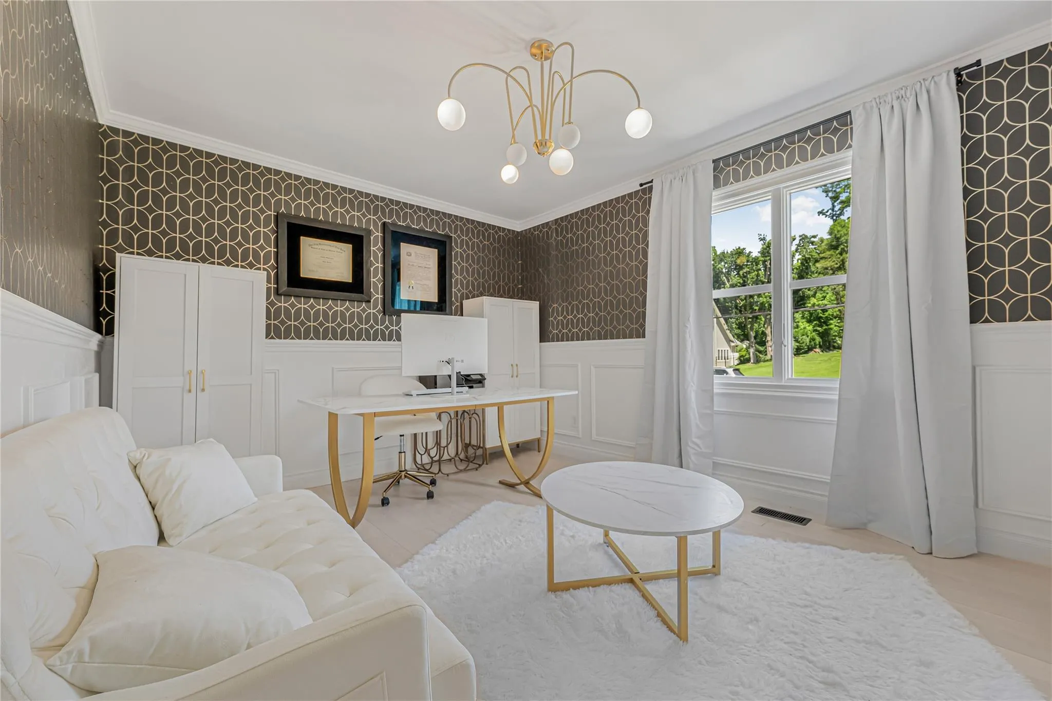 Living room with wallpapered walls, crown molding, wainscoting, an office area, and a chandelier Living room with wallpapered walls, crown molding, wainscoting, an office area, and a chandelier