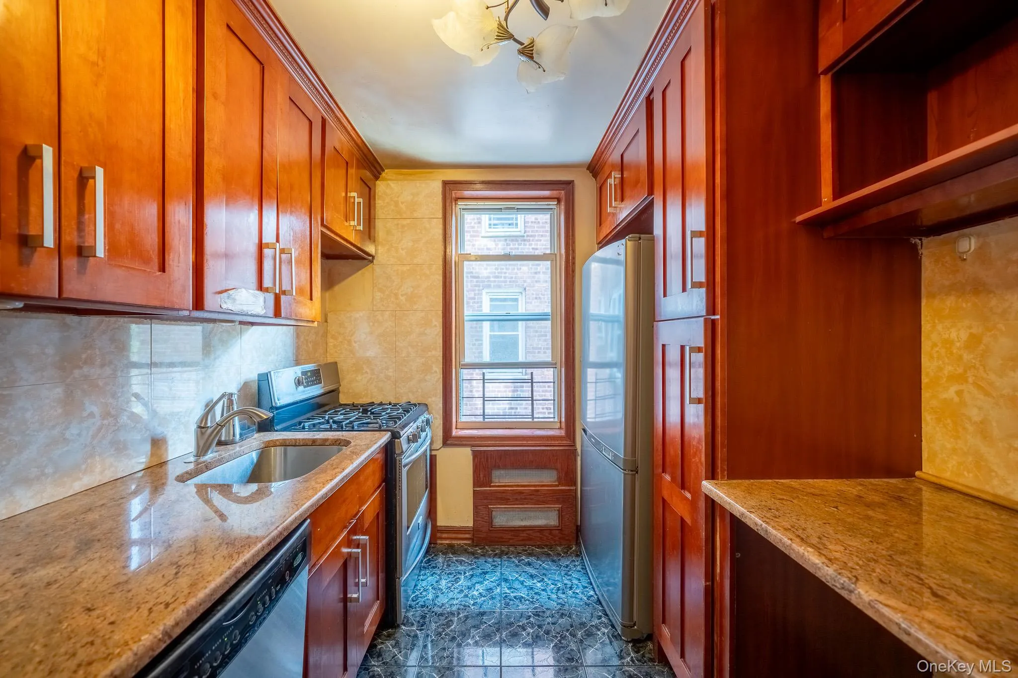 Kitchen with stainless steel appliances, light stone countertops, decorative backsplash, brown cabinetry, and a chandelier Kitchen with stainless steel appliances, light stone countertops, decorative backsplash, brown cabinetry, and a chandelier