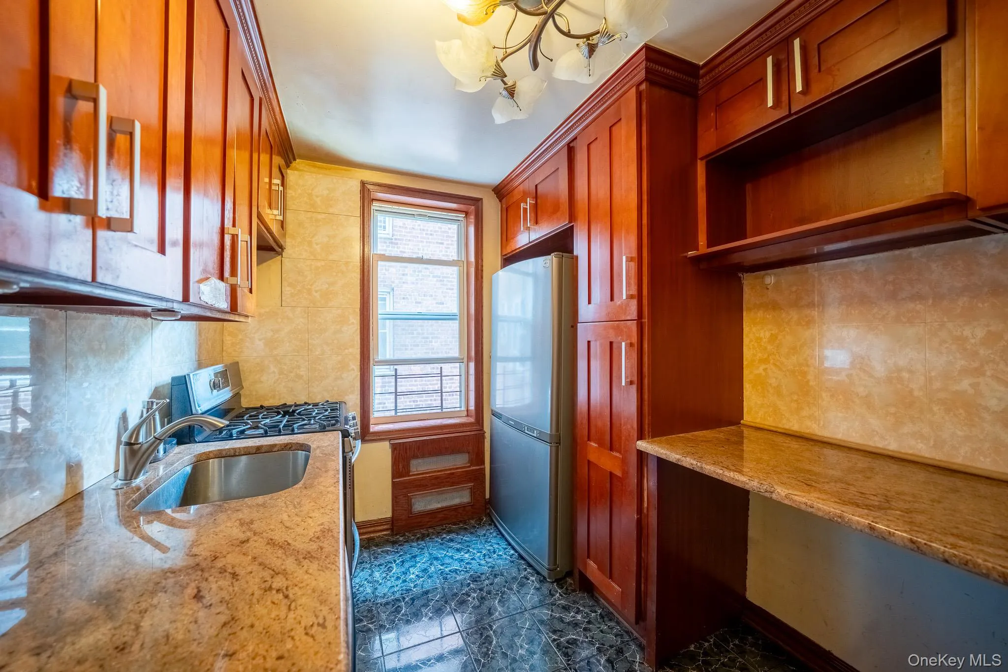 Kitchen featuring freestanding refrigerator, a chandelier, stainless steel gas stove, decorative backsplash, and light stone countertops Kitchen featuring freestanding refrigerator, a chandelier, stainless steel gas stove, decorative backsplash, and light stone countertops