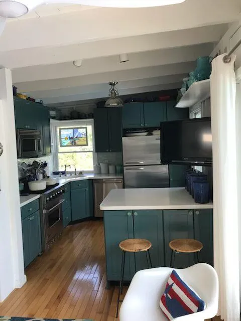 Kitchen featuring appliances with stainless steel finishes, hardwood / wood-style floors, light countertops, a peninsula, and blue cabinetry Kitchen featuring appliances with stainless steel finishes, hardwood / wood-style floors, light countertops, a peninsula, and blue cabinetry