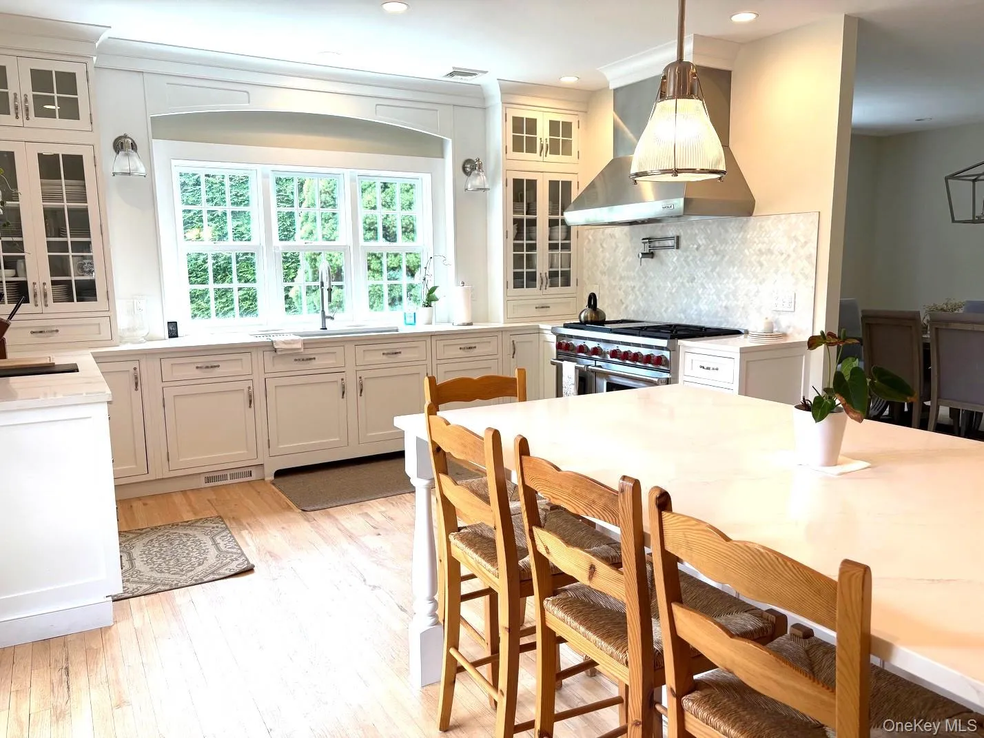 Kitchen featuring double oven range, tasteful backsplash, light wood finished floors, wall chimney exhaust hood, and hanging light fixtures Kitchen featuring double oven range, tasteful backsplash, light wood finished floors, wall chimney exhaust hood, and hanging light fixtures