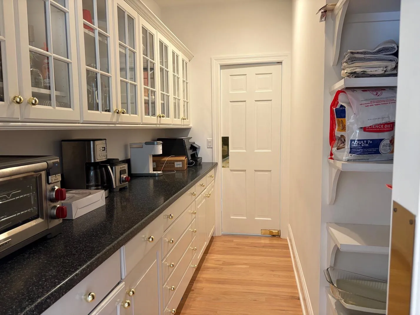Kitchen featuring light wood-style floors, dark stone countertops, and glass insert cabinets Kitchen featuring light wood-style floors, dark stone countertops, and glass insert cabinets