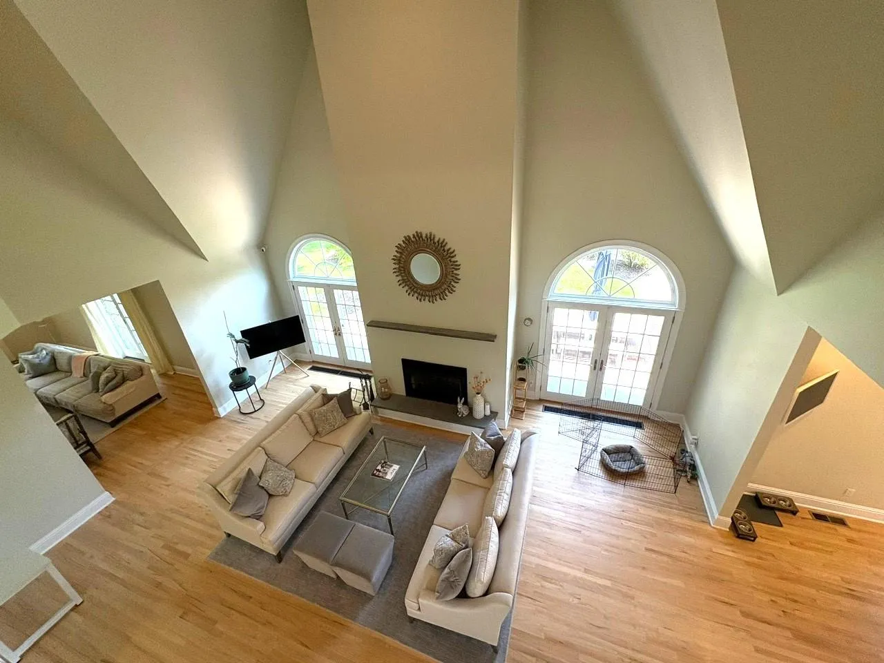 Living room with a fireplace, a towering ceiling, light wood-style floors, healthy amount of natural light, and french doors Living room with a fireplace, a towering ceiling, light wood-style floors, healthy amount of natural light, and french doors