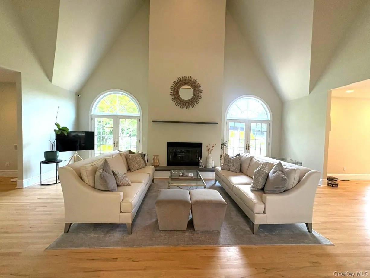 Living area featuring high vaulted ceiling, wood finished floors, healthy amount of natural light, a fireplace, and french doors Living area featuring high vaulted ceiling, wood finished floors, healthy amount of natural light, a fireplace, and french doors