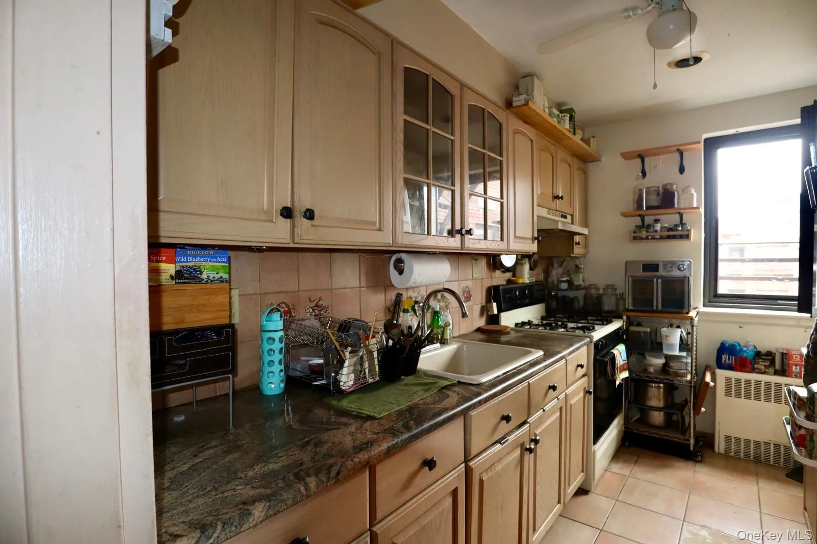 Kitchen with radiator, white gas stove, under cabinet range hood, light tile patterned floors, and glass insert cabinets Kitchen with radiator, white gas stove, under cabinet range hood, light tile patterned floors, and glass insert cabinets