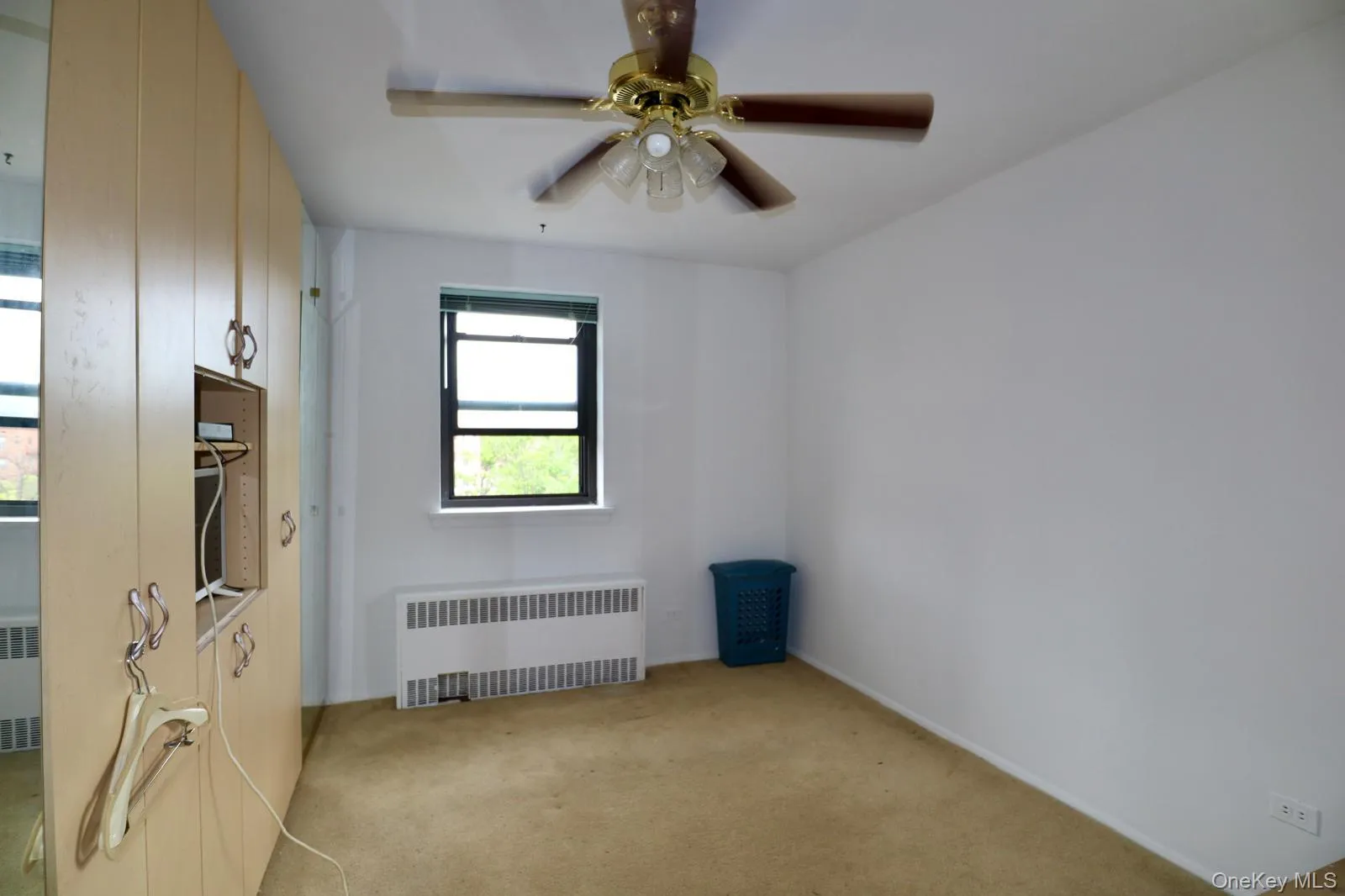 Unfurnished room with radiator, light colored carpet, and a ceiling fan Unfurnished room with radiator, light colored carpet, and a ceiling fan