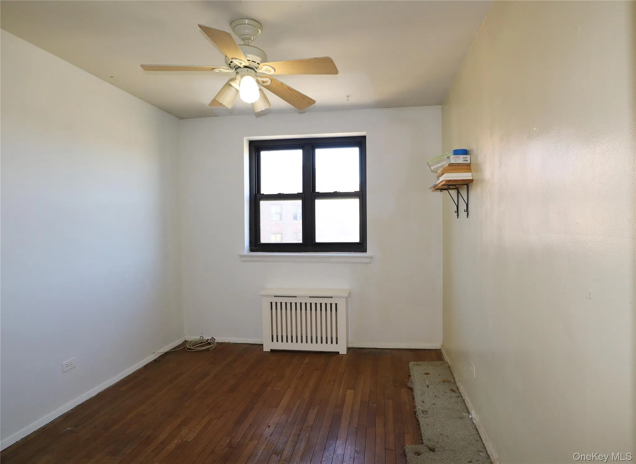 Spare room featuring dark wood-style flooring, radiator heating unit, and ceiling fan Spare room featuring dark wood-style flooring, radiator heating unit, and ceiling fan