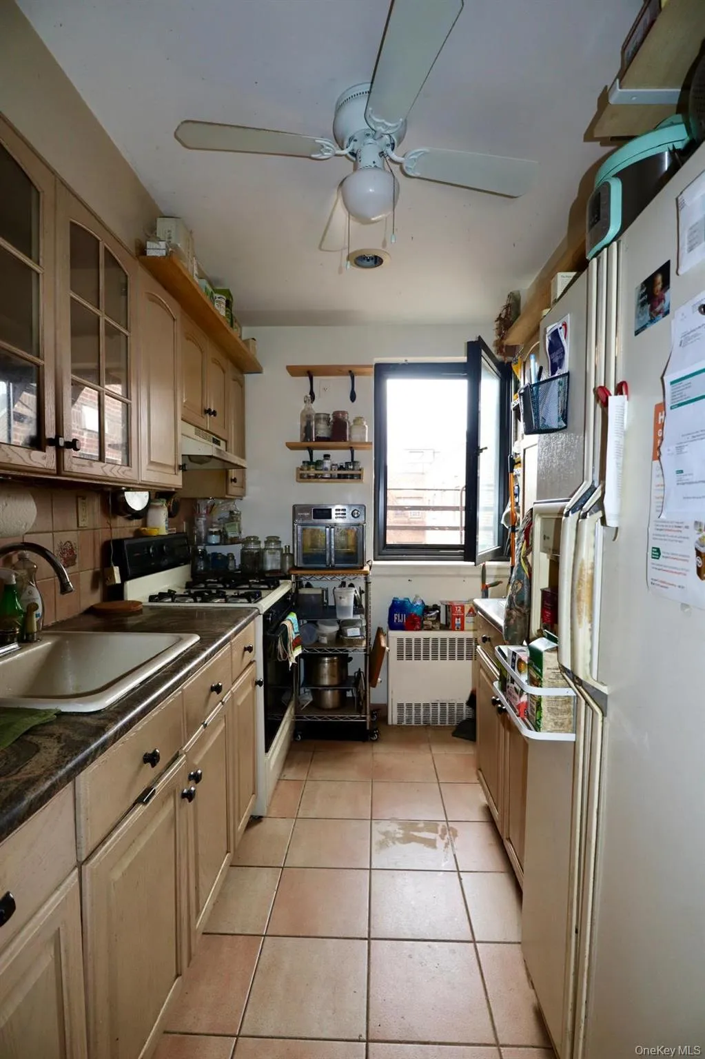 Kitchen with white appliances, radiator, under cabinet range hood, dark countertops, and a ceiling fan Kitchen with white appliances, radiator, under cabinet range hood, dark countertops, and a ceiling fan