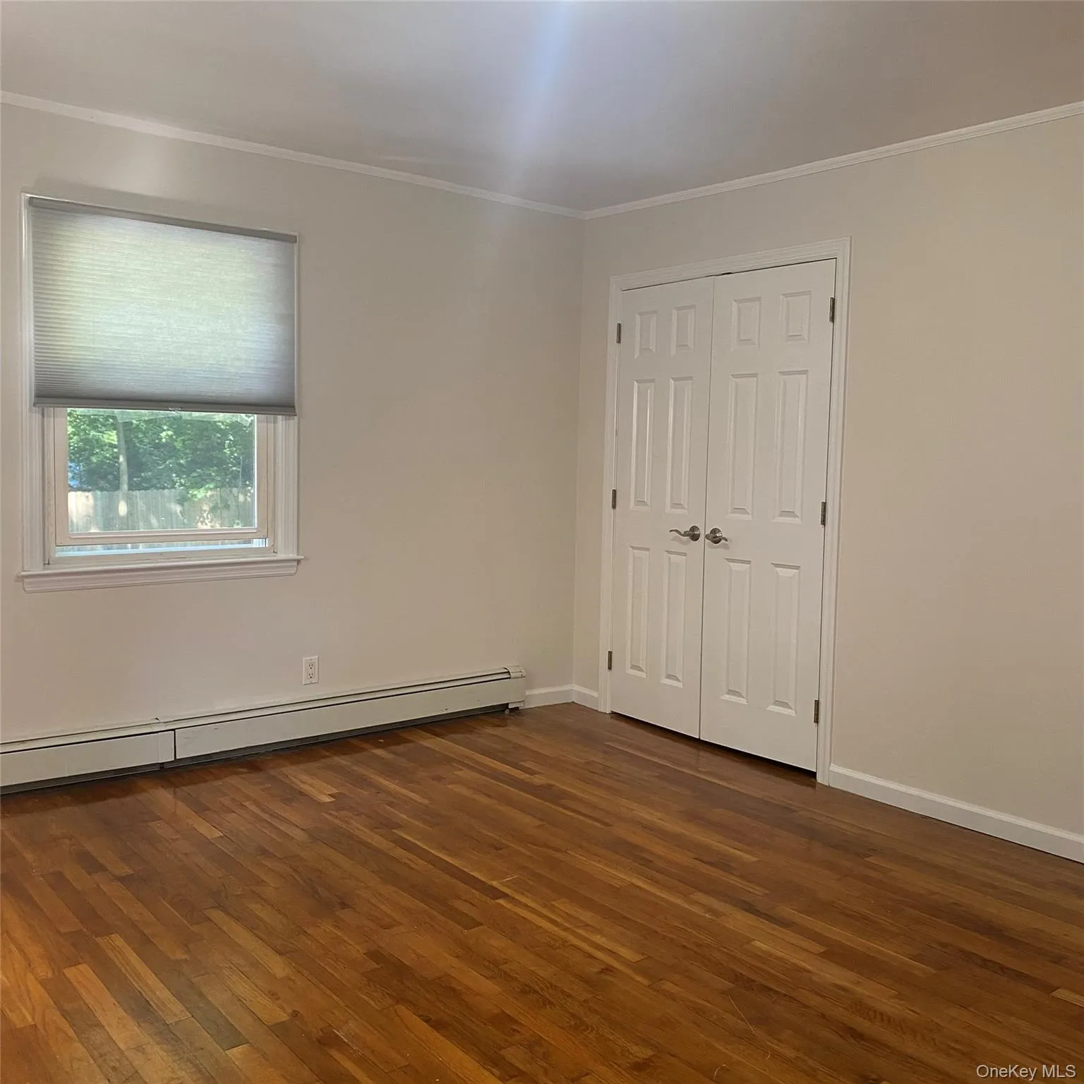 Queen size bedroom featuring a baseboard heating unit, dark wood-style flooring, crown molding, and a closet Queen size bedroom featuring a baseboard heating unit, dark wood-style flooring, crown molding, and a closet