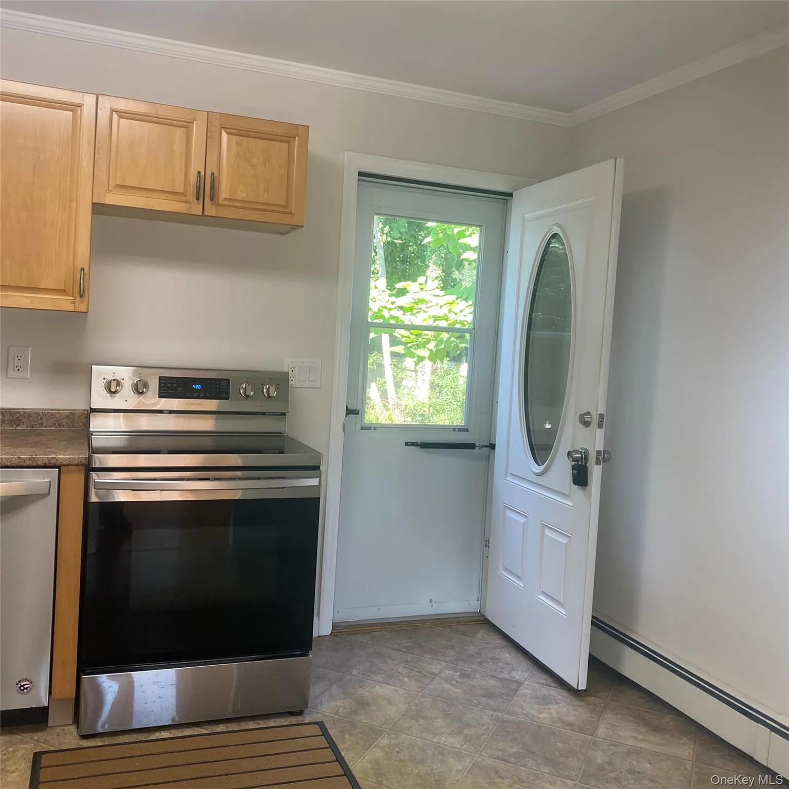 Kitchen with appliances with stainless steel finishes, a baseboard radiator, ornamental molding, light brown cabinets, and dark countertops Kitchen with appliances with stainless steel finishes, a baseboard radiator, ornamental molding, light brown cabinets, and dark countertops